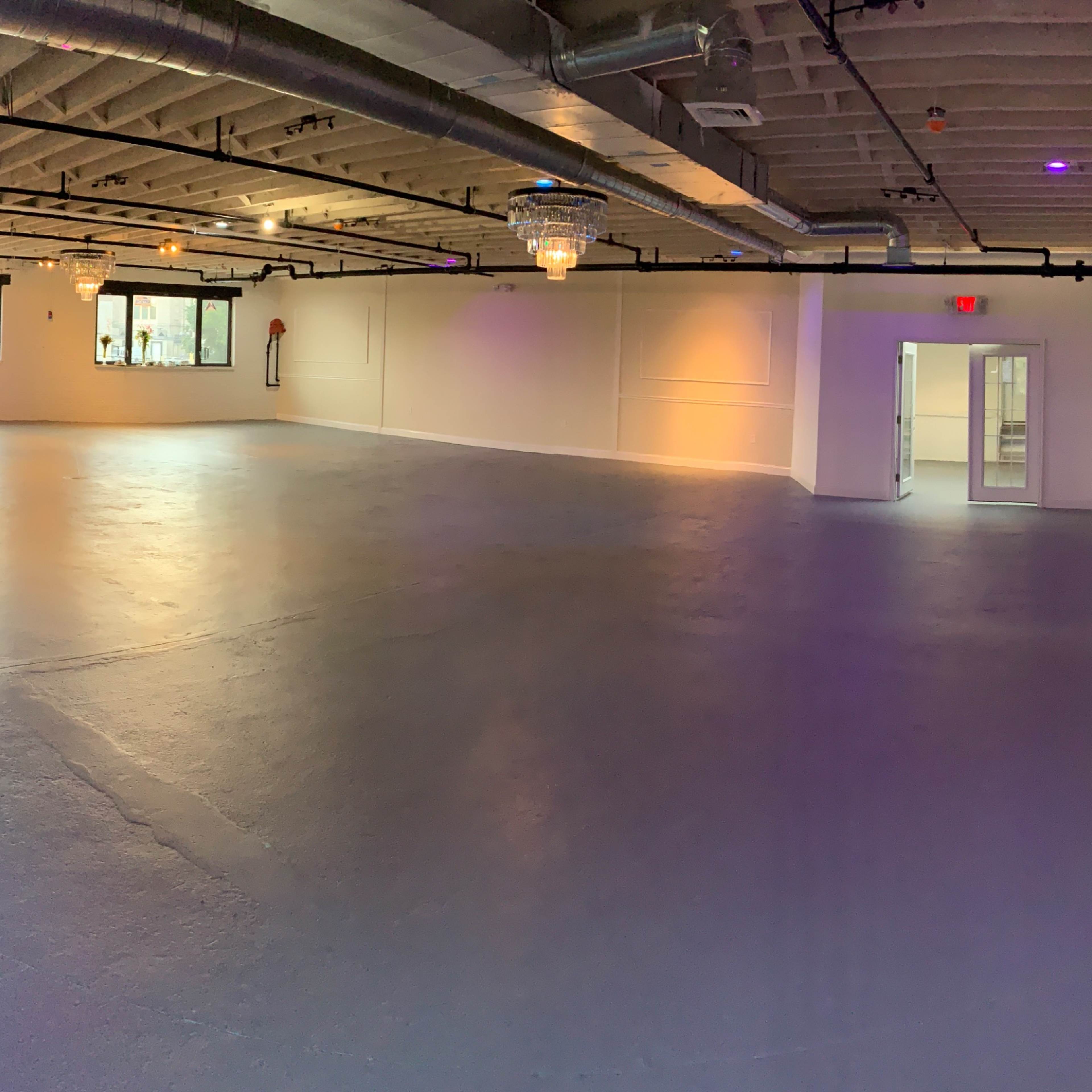 A spacious, empty room with large windows, fluorescent lighting, and a smooth concrete floor.