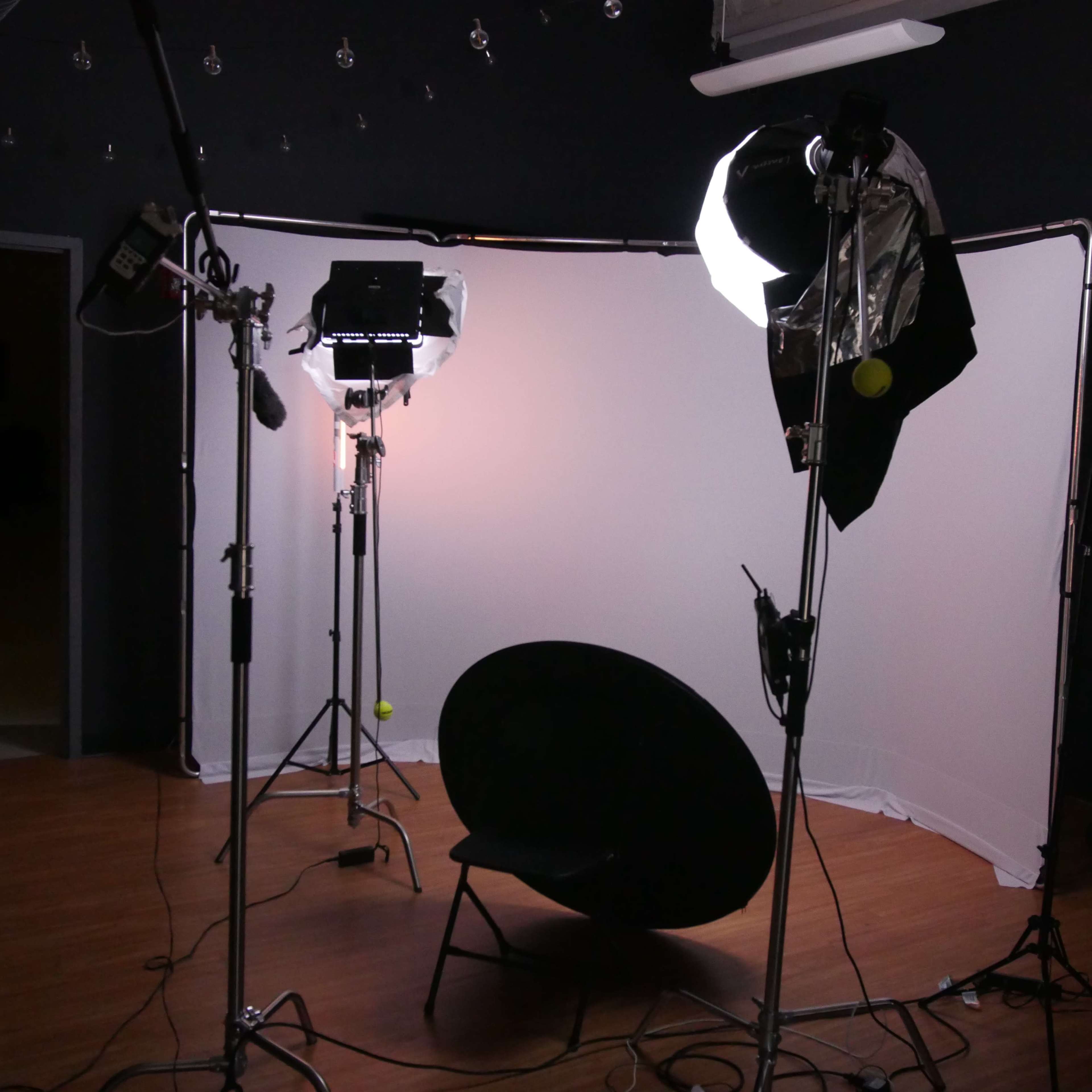 A photography studio setup with lights, stands, and a black chair positioned in front of a white backdrop.