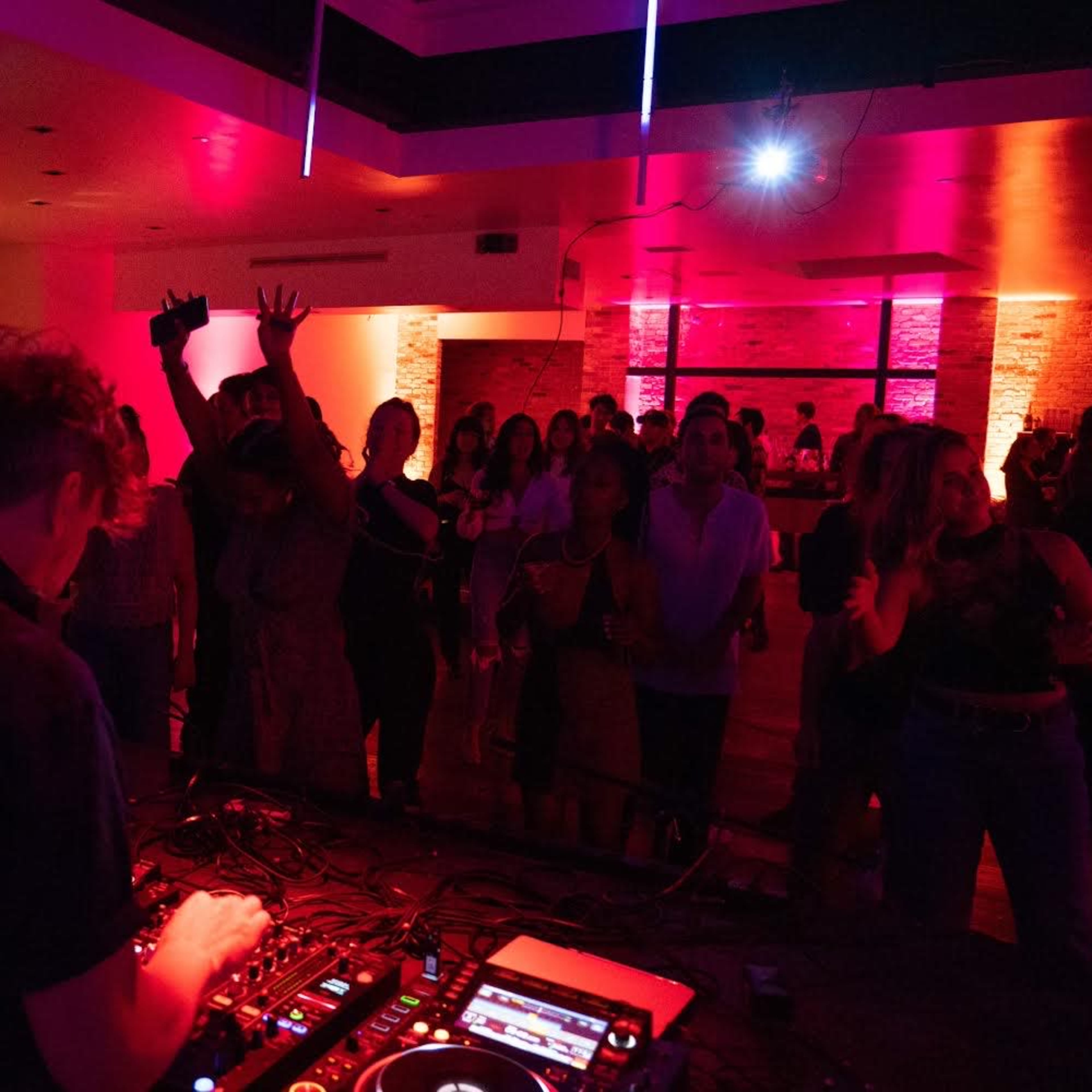 A DJ performs in a dimly lit venue with colorful lights while an engaged crowd watches and enjoys the music.