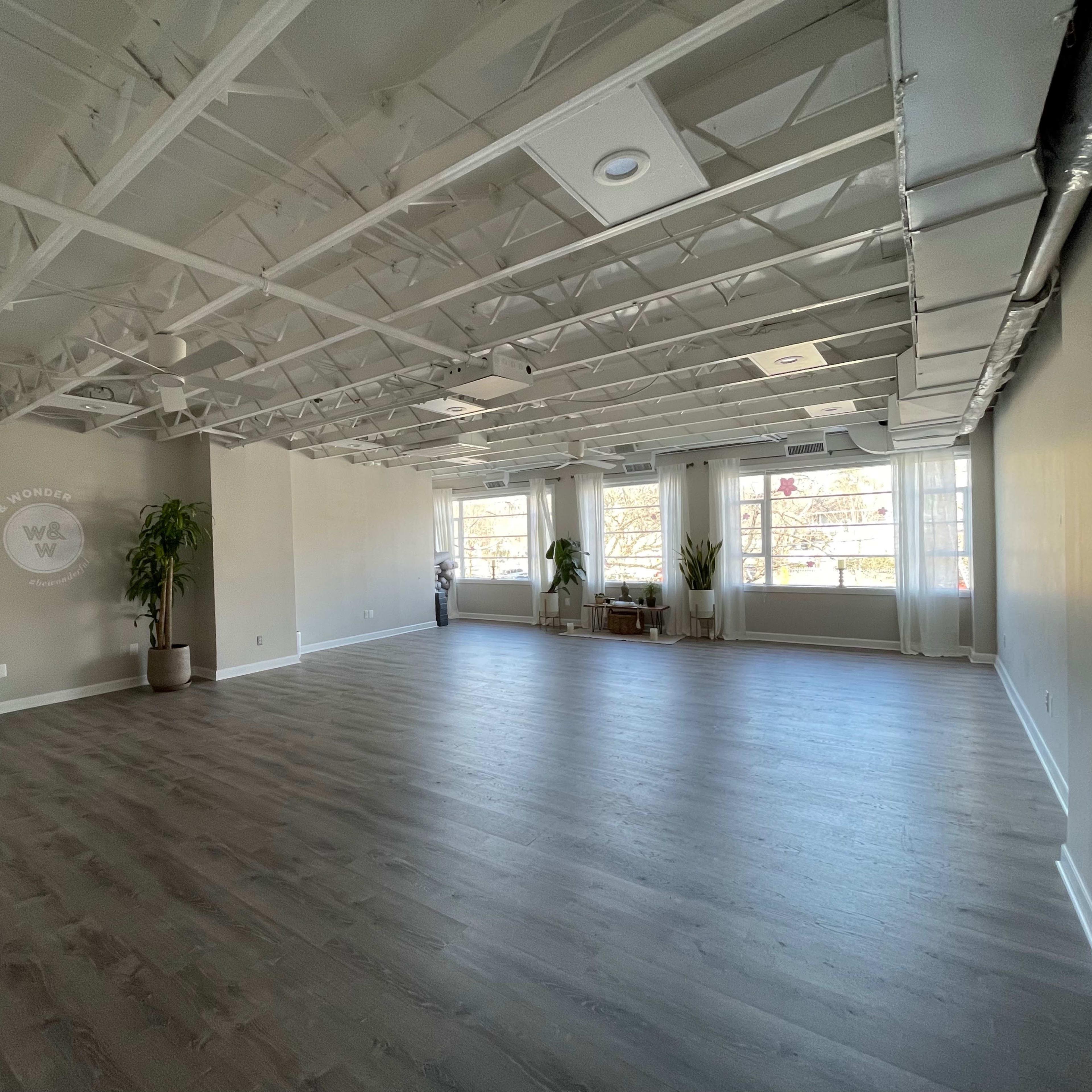 A spacious, empty interior room with large windows and exposed ceiling beams.