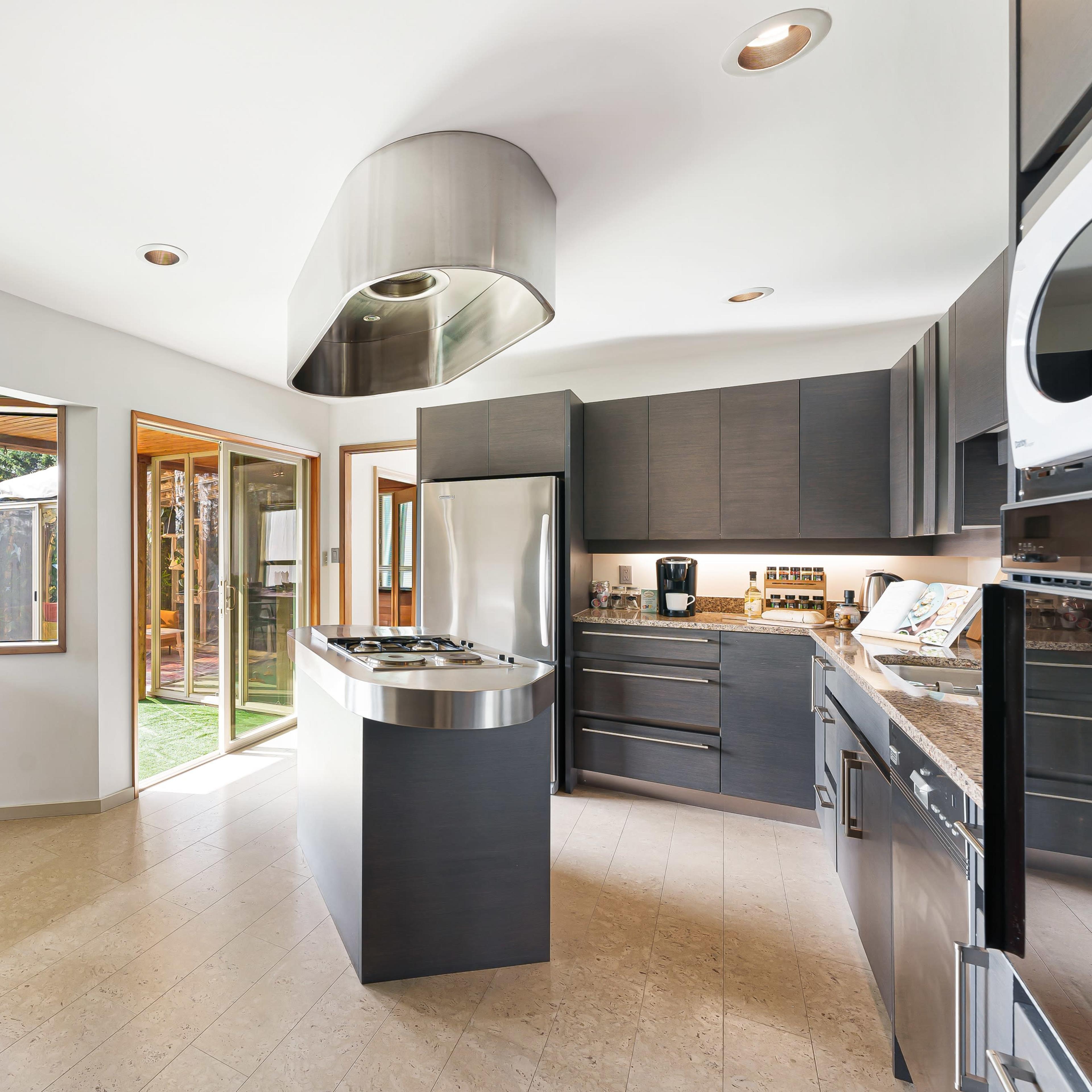 A modern kitchen features sleek cabinets, a central island with a stovetop, and large windows that allow natural light to fill the space.