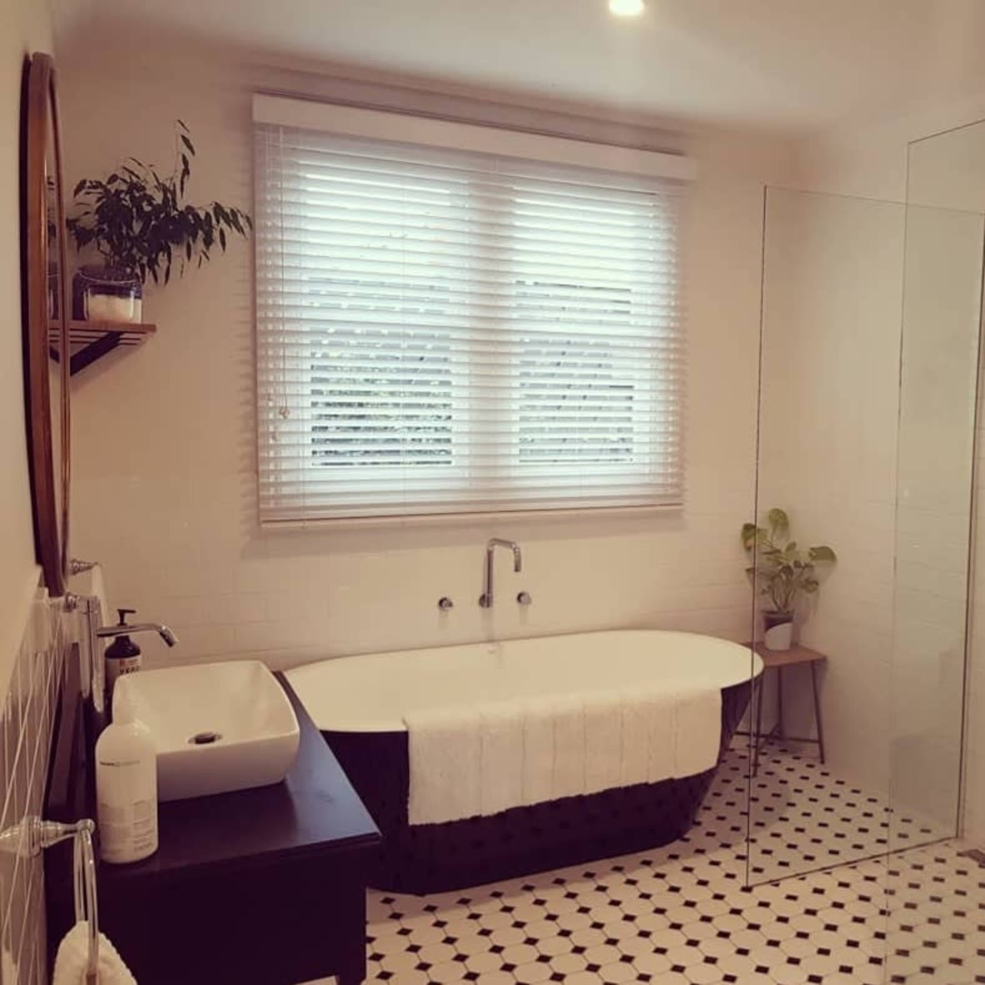 A modern bathroom featuring a freestanding bathtub, a glass shower enclosure, and a window with blinds.