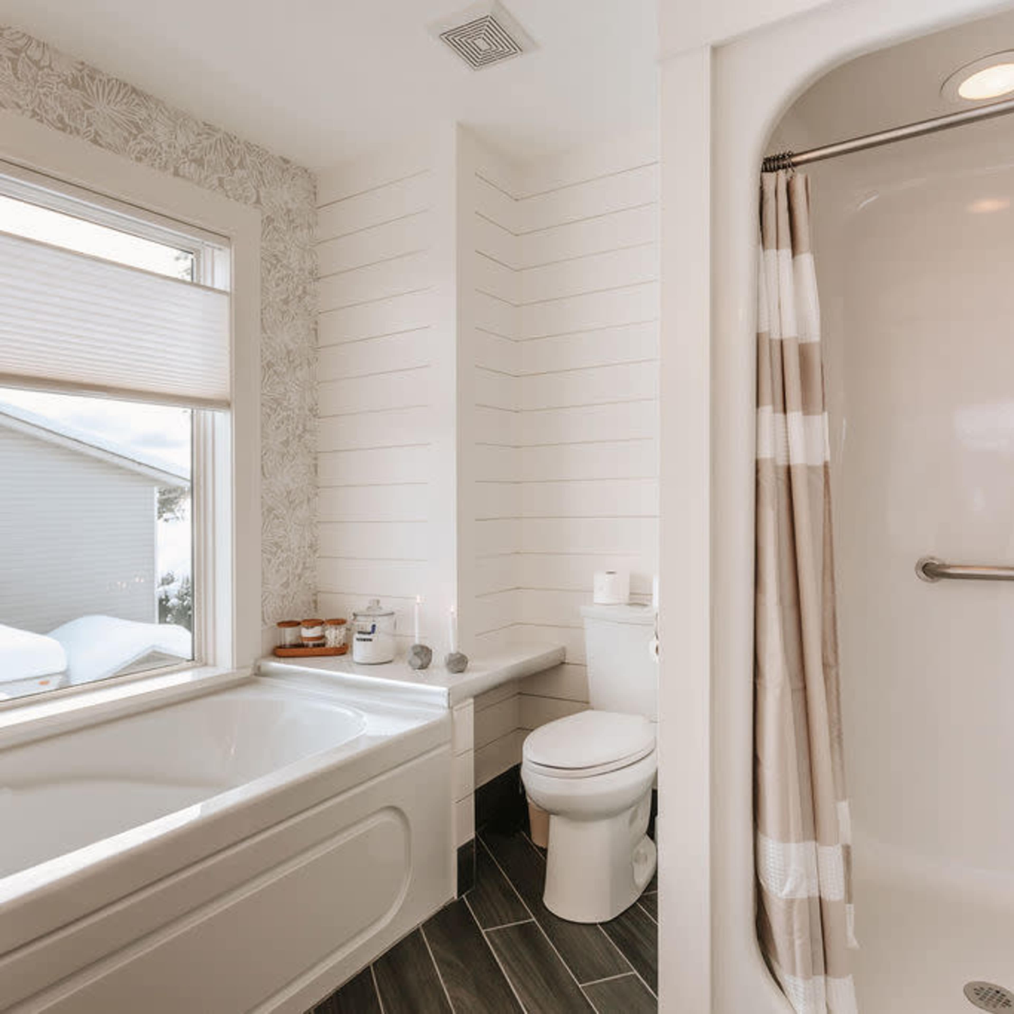 A modern bathroom featuring a bathtub, a shower stall, a toilet, and a window with a snowy view outside.
