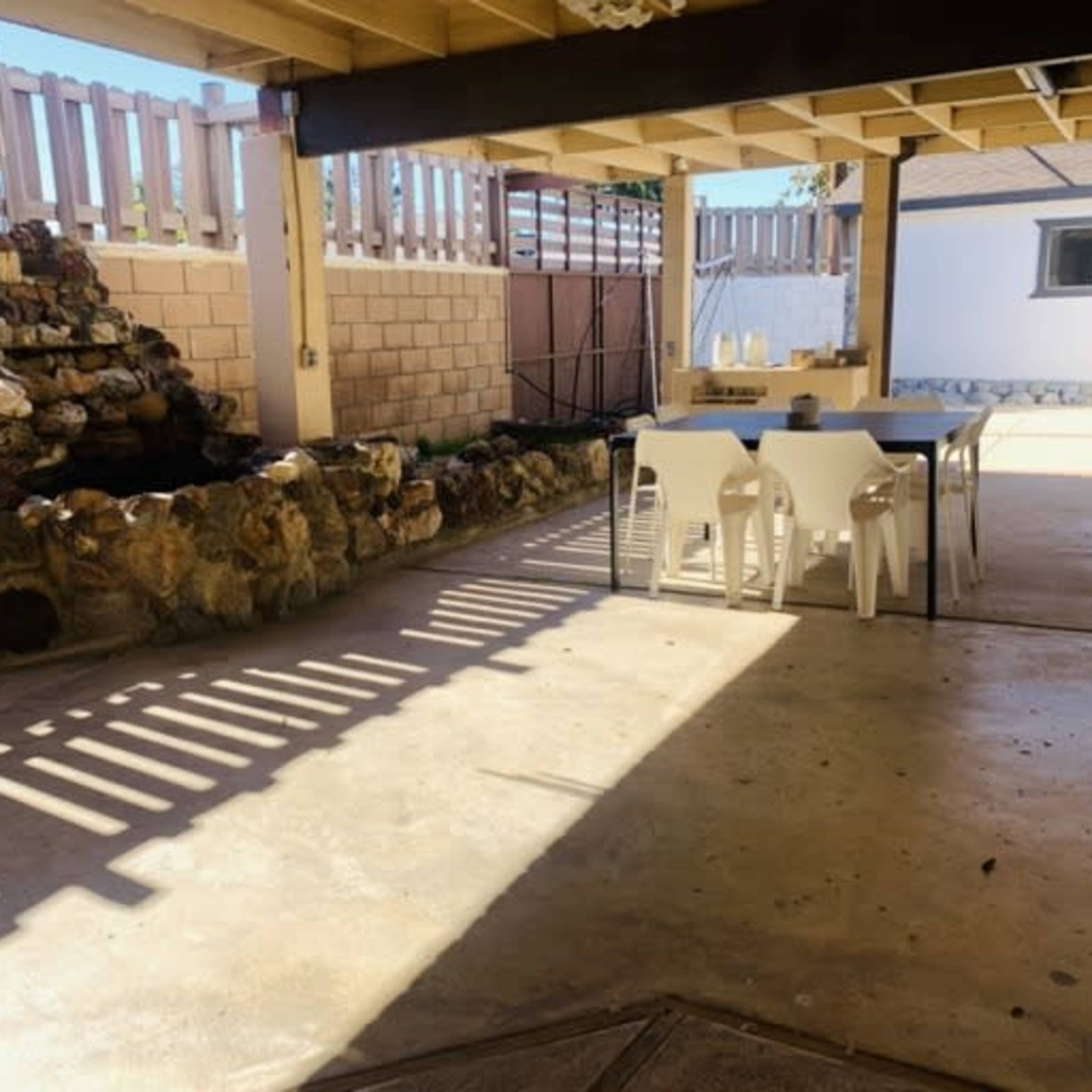 A shaded outdoor patio area featuring a stone fountain, a table with chairs, and a concrete floor.