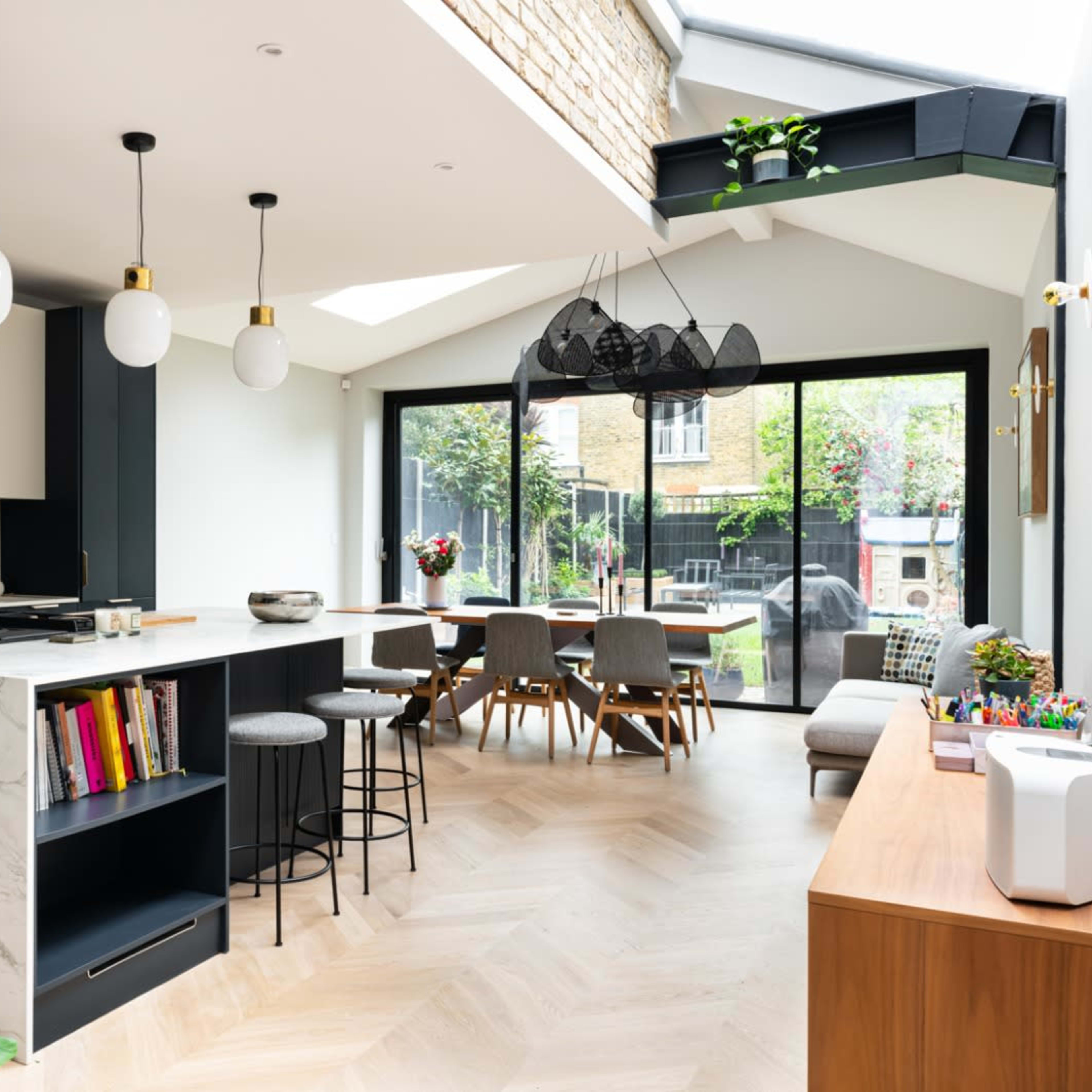A modern kitchen and dining area featuring a marble countertop, pendant lighting, and a large window that opens to a garden.