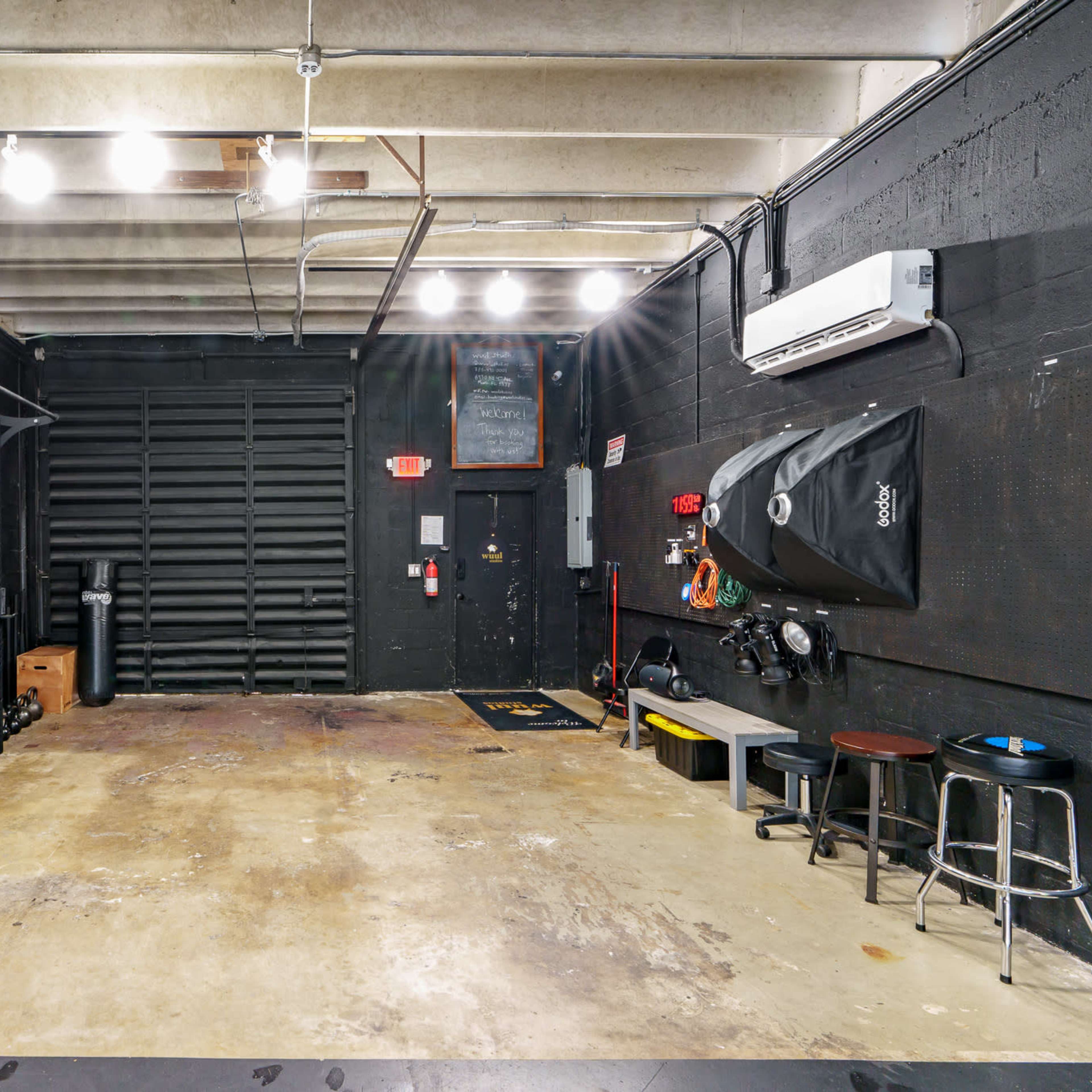 A gym space with black walls, exercise equipment along one side, and a concrete floor.