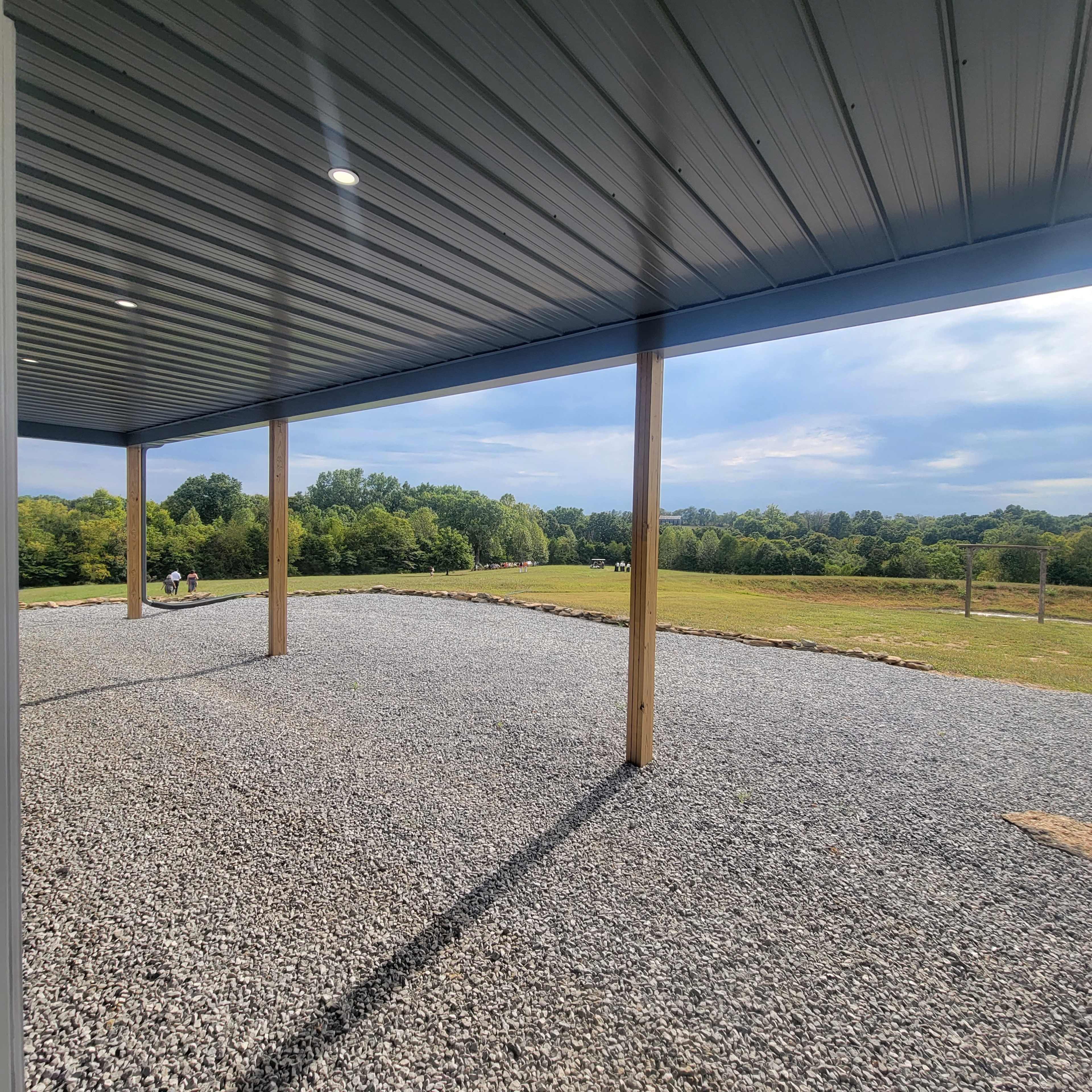 A gravel area under a covered porch with a view of a green landscape and trees in the distance.