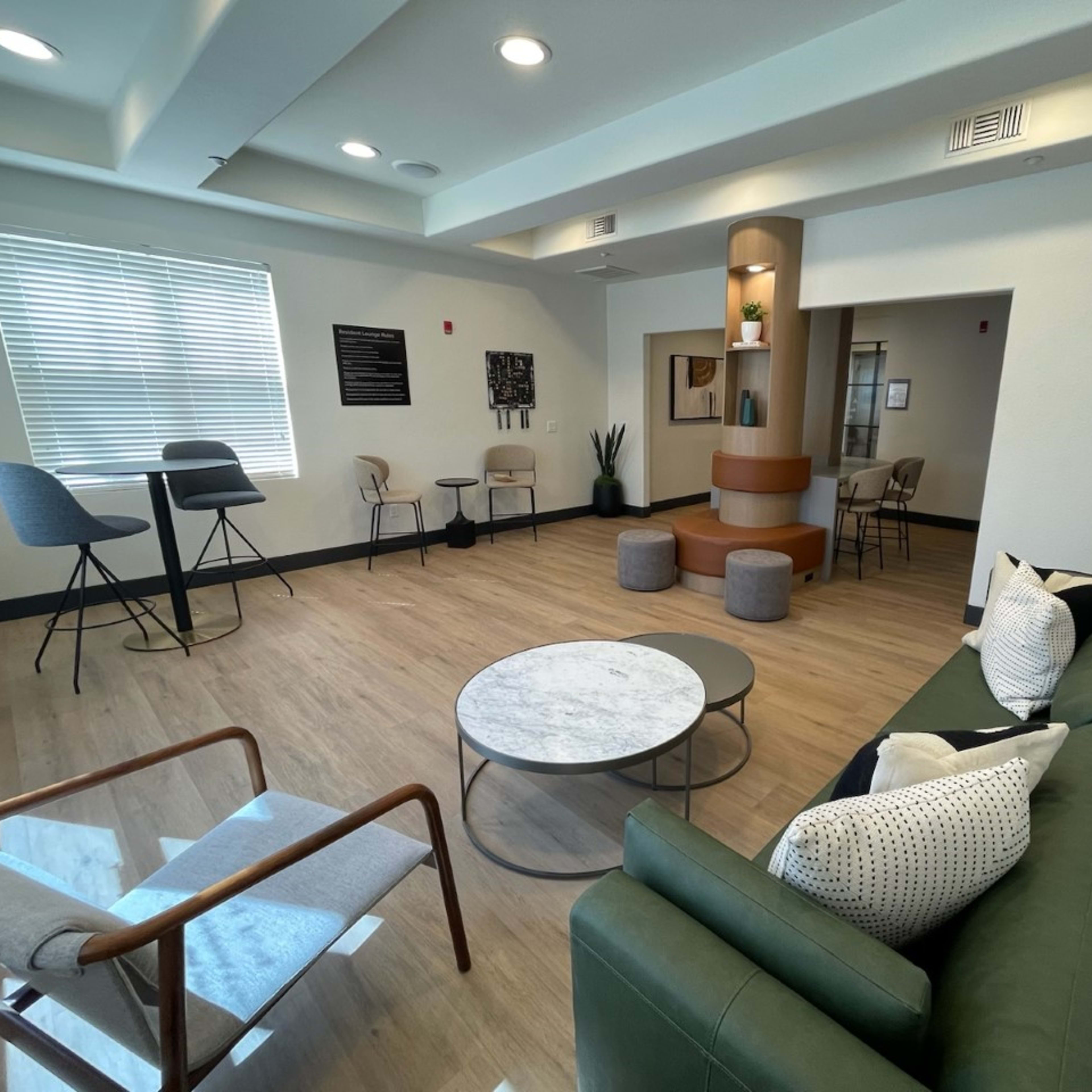 A modern lounge area featuring a green sofa, a marble coffee table, several chairs, and a small bar table.