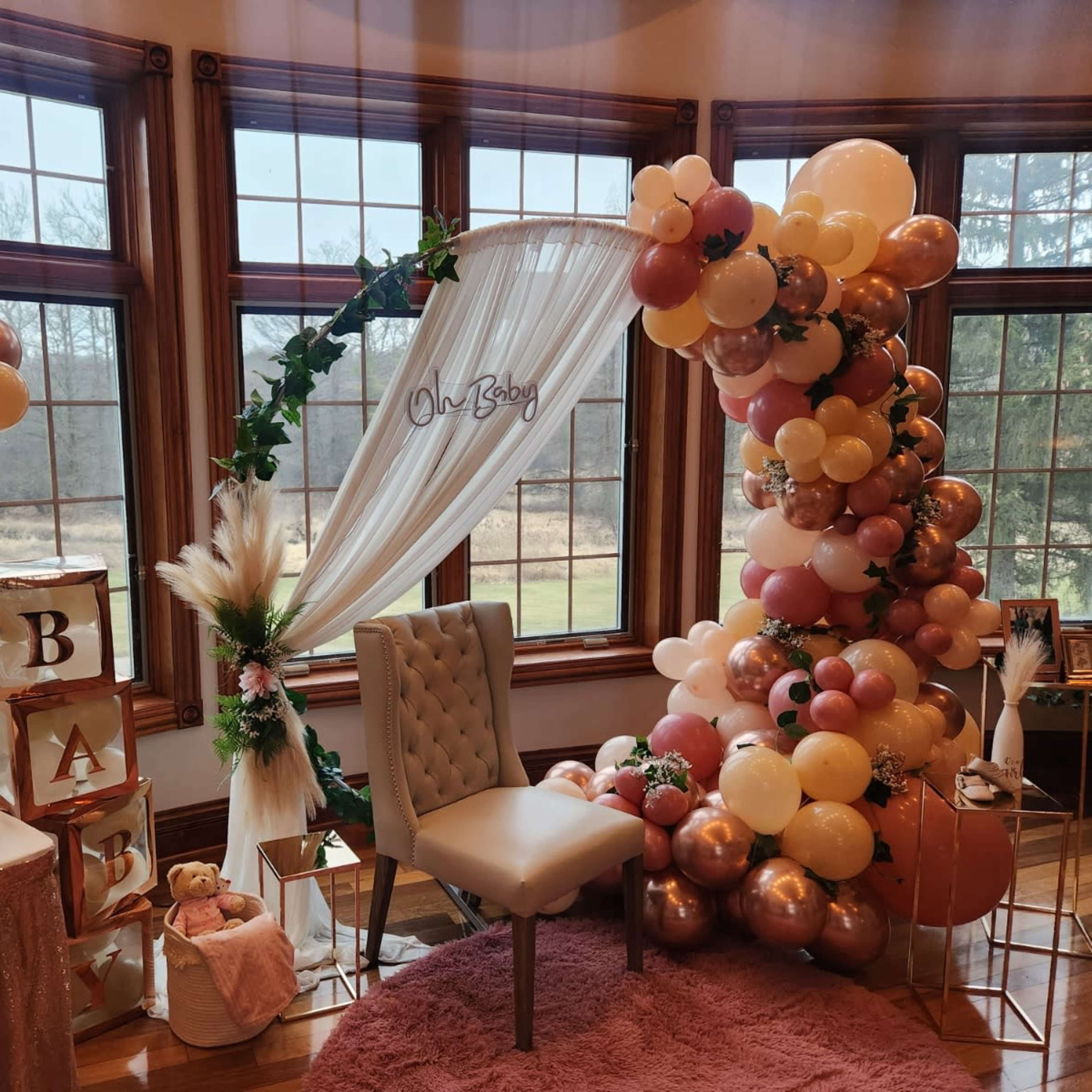 A decorated room with a backdrop of balloons, a small chair, and a table adorned with baby-themed decor for a celebration.