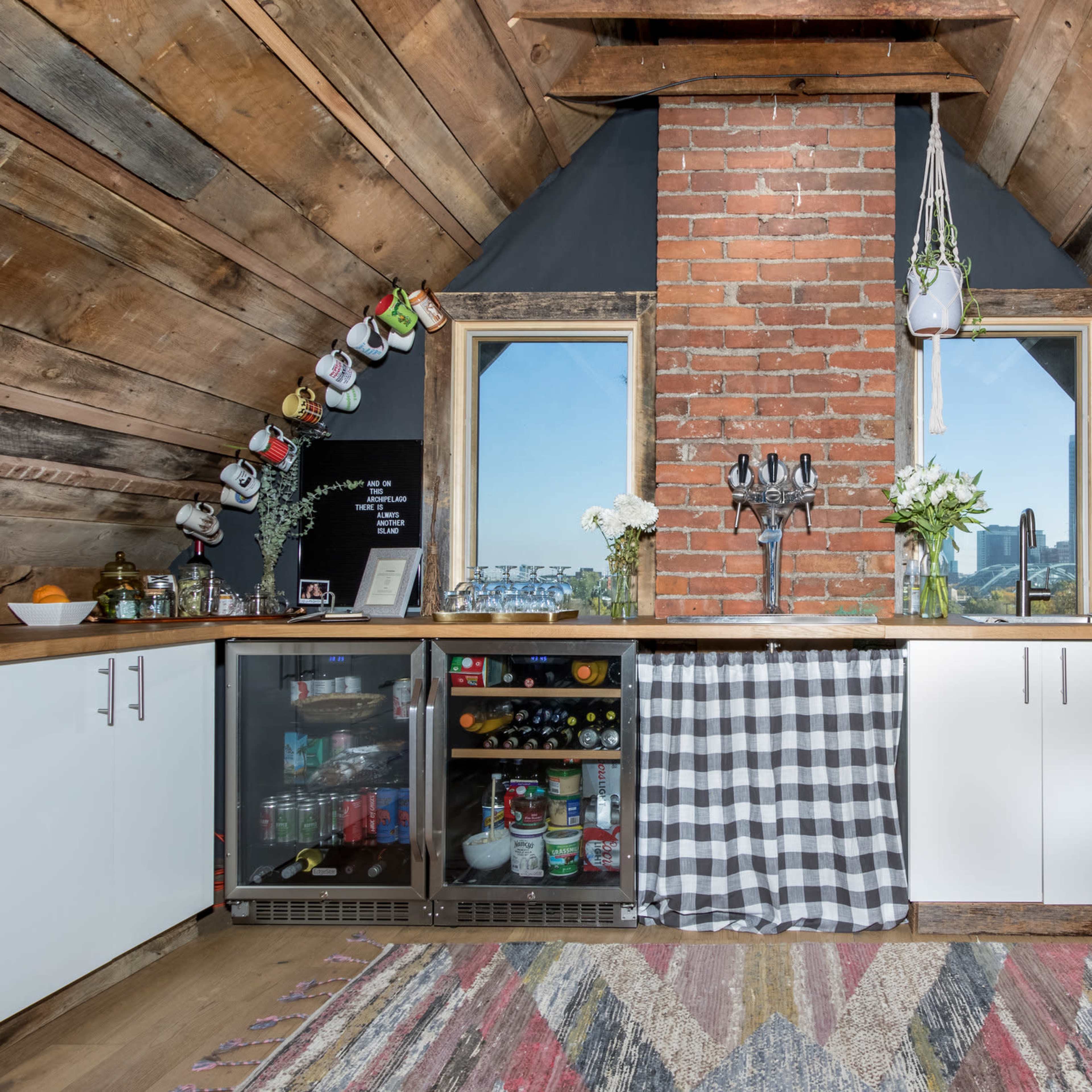 A cozy attic kitchen featuring a brick accent wall, wooden beams, and a mix of modern appliances and rustic decor.