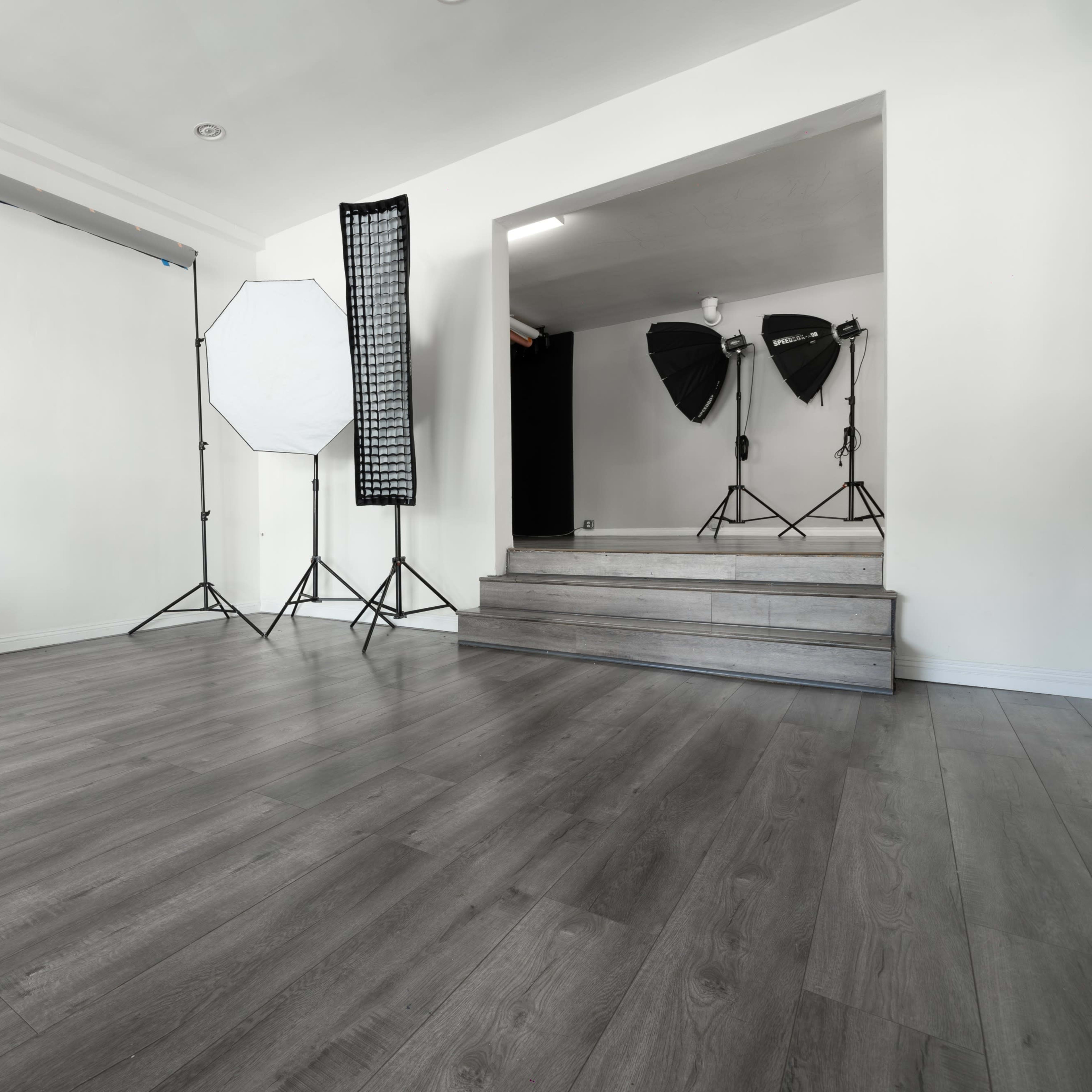 A well-lit photography studio with a blank backdrop, light stands, and a staircase leading to another area.