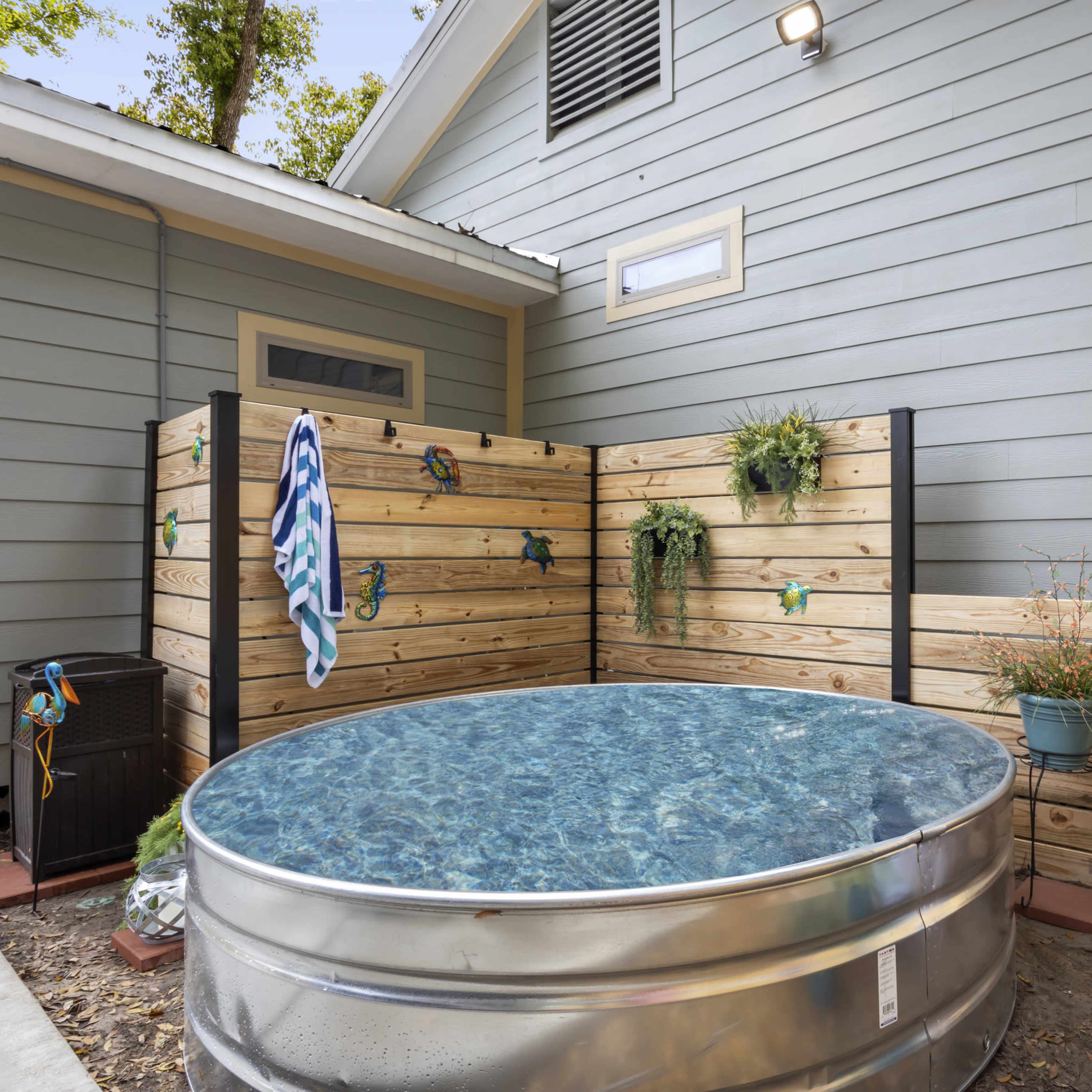 A small outdoor area with a round, metallic above-ground pool enclosed by wooden fencing and decorated with potted plants.