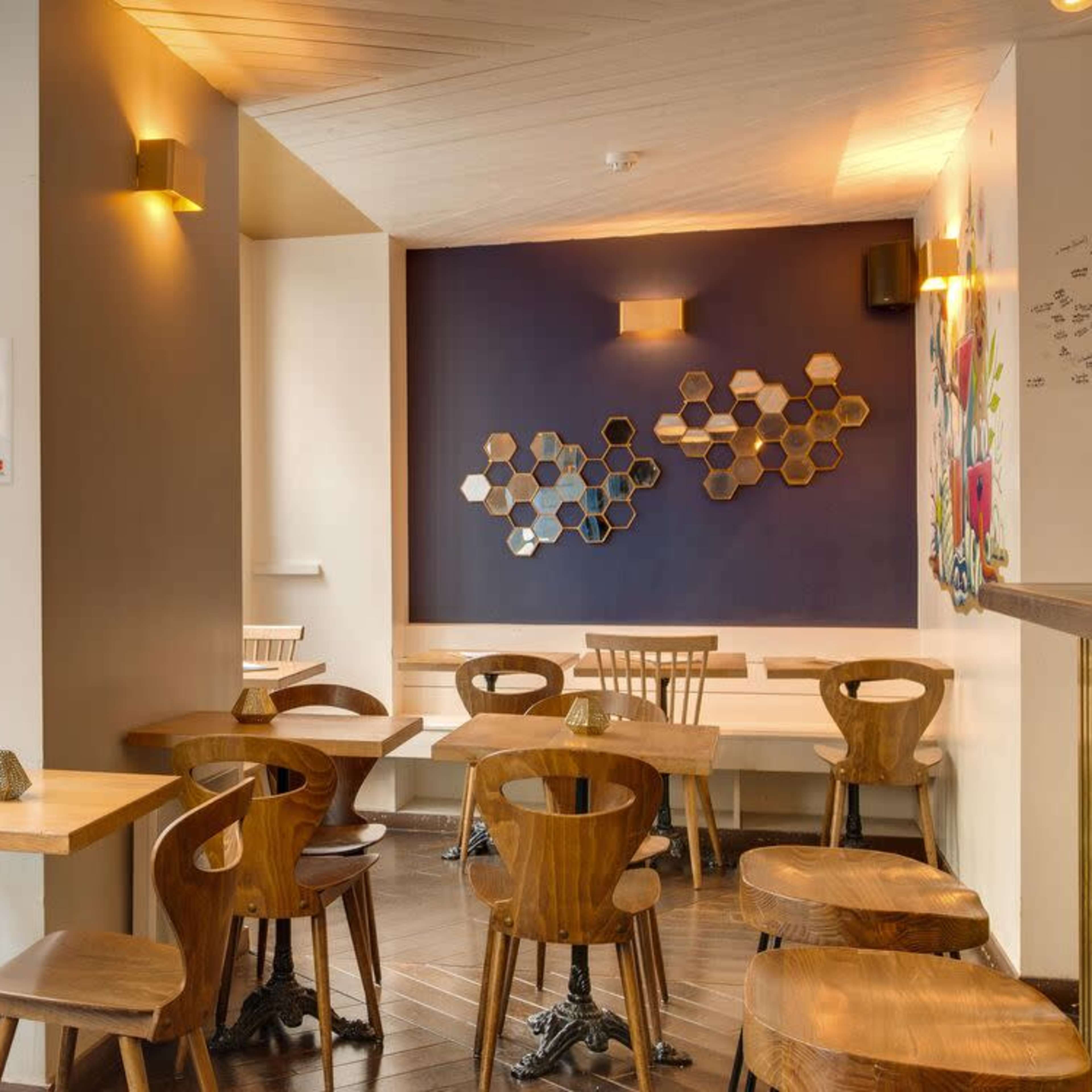A modern café interior with wooden tables and chairs, a colorful wall design, and a bar area on the right.