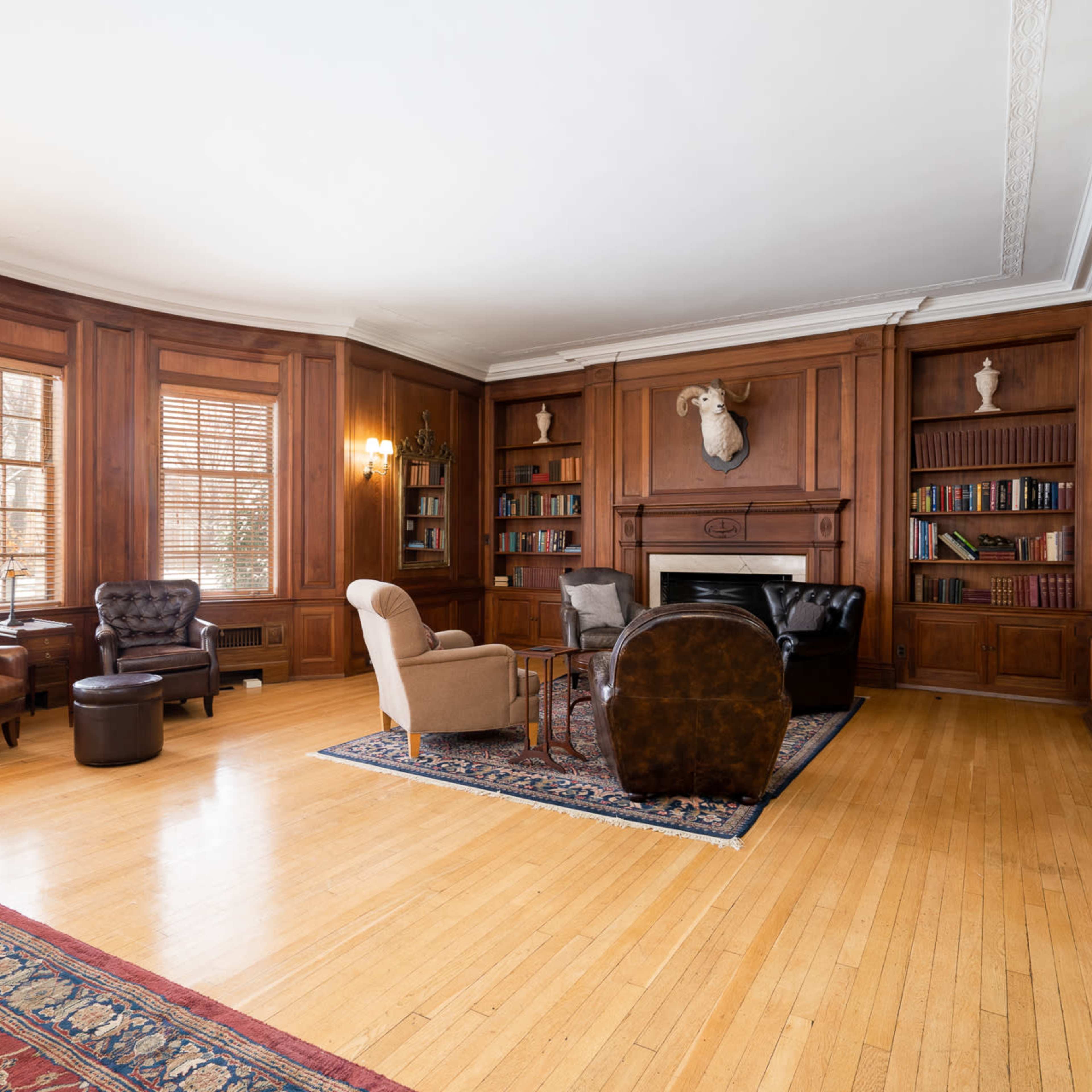 The room features wood-paneled walls, a fireplace, a variety of seating options, and a large area rug on hardwood flooring.