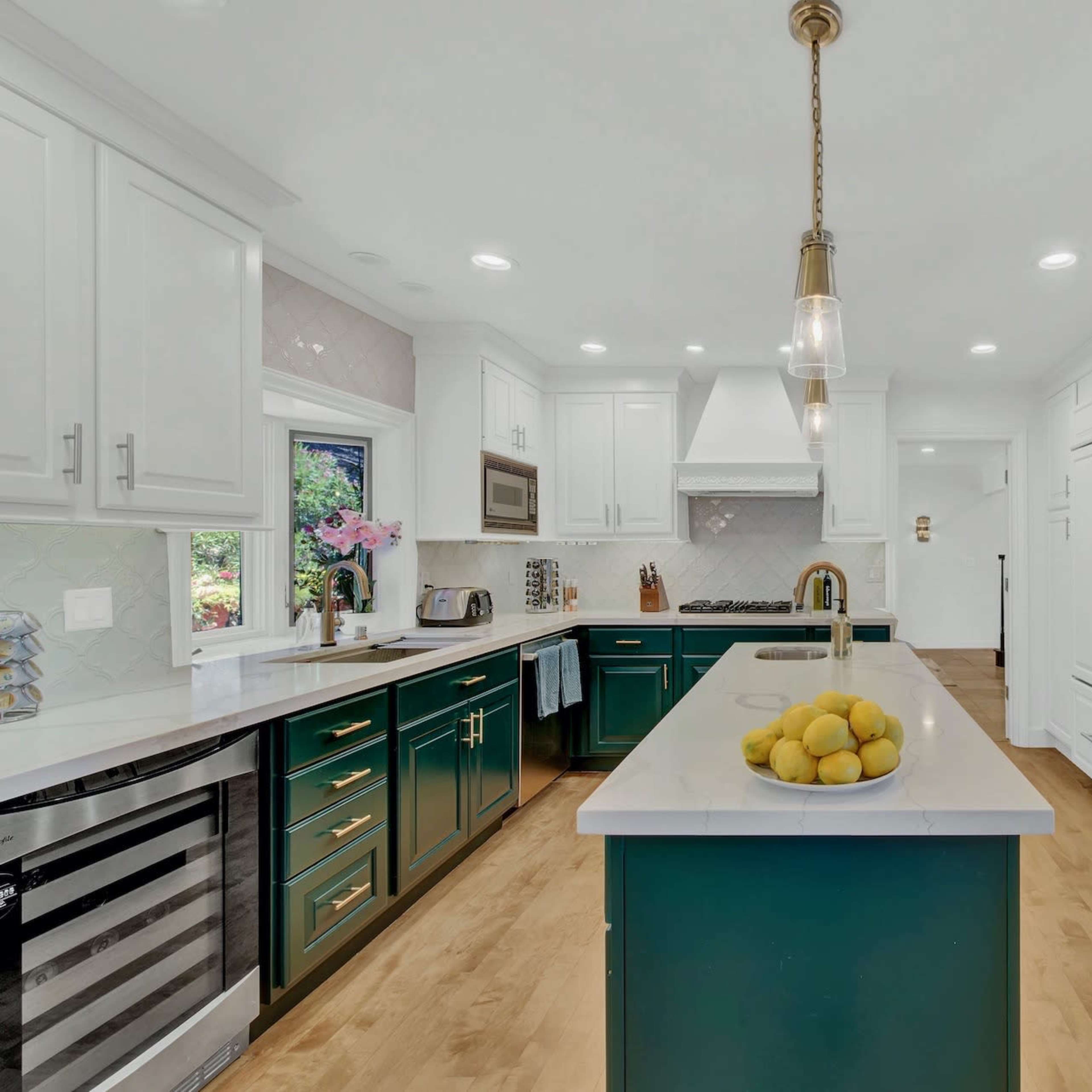 A modern kitchen features white cabinets, a central island with a green base, and stainless steel appliances.
