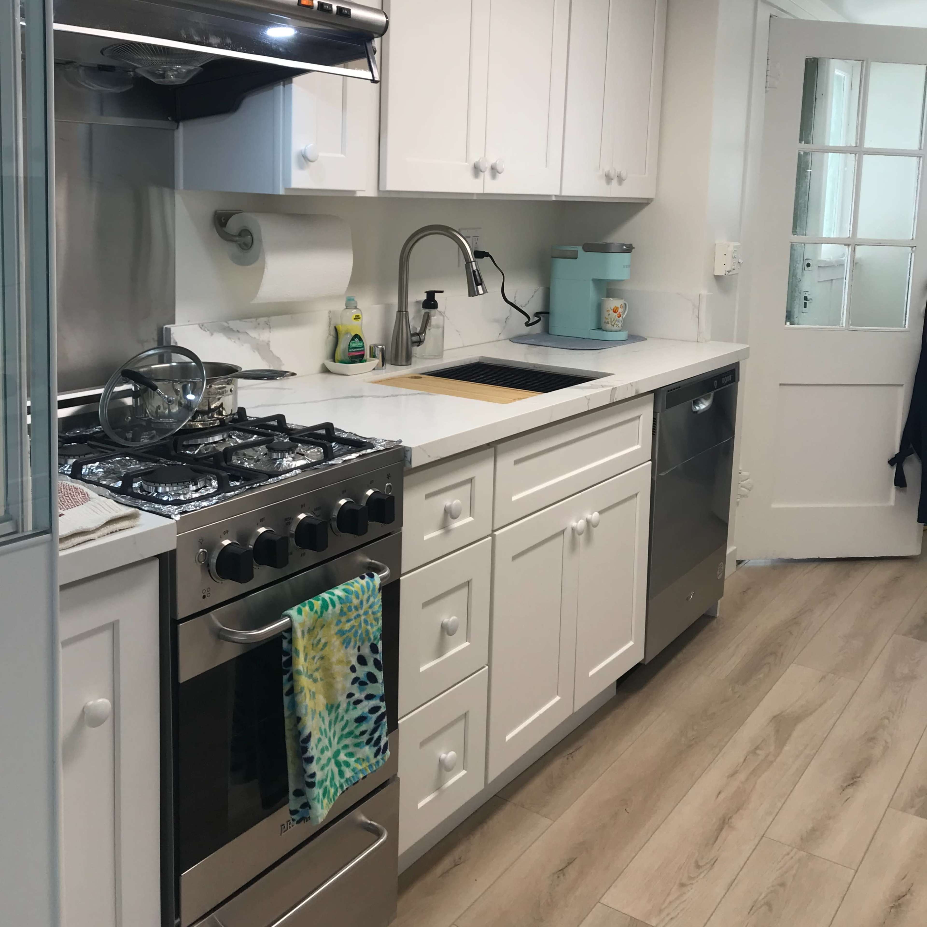 A compact kitchen features white cabinets, a stainless steel stove, and a sink with a modern faucet, alongside a dishwasher and a door leading to another room.