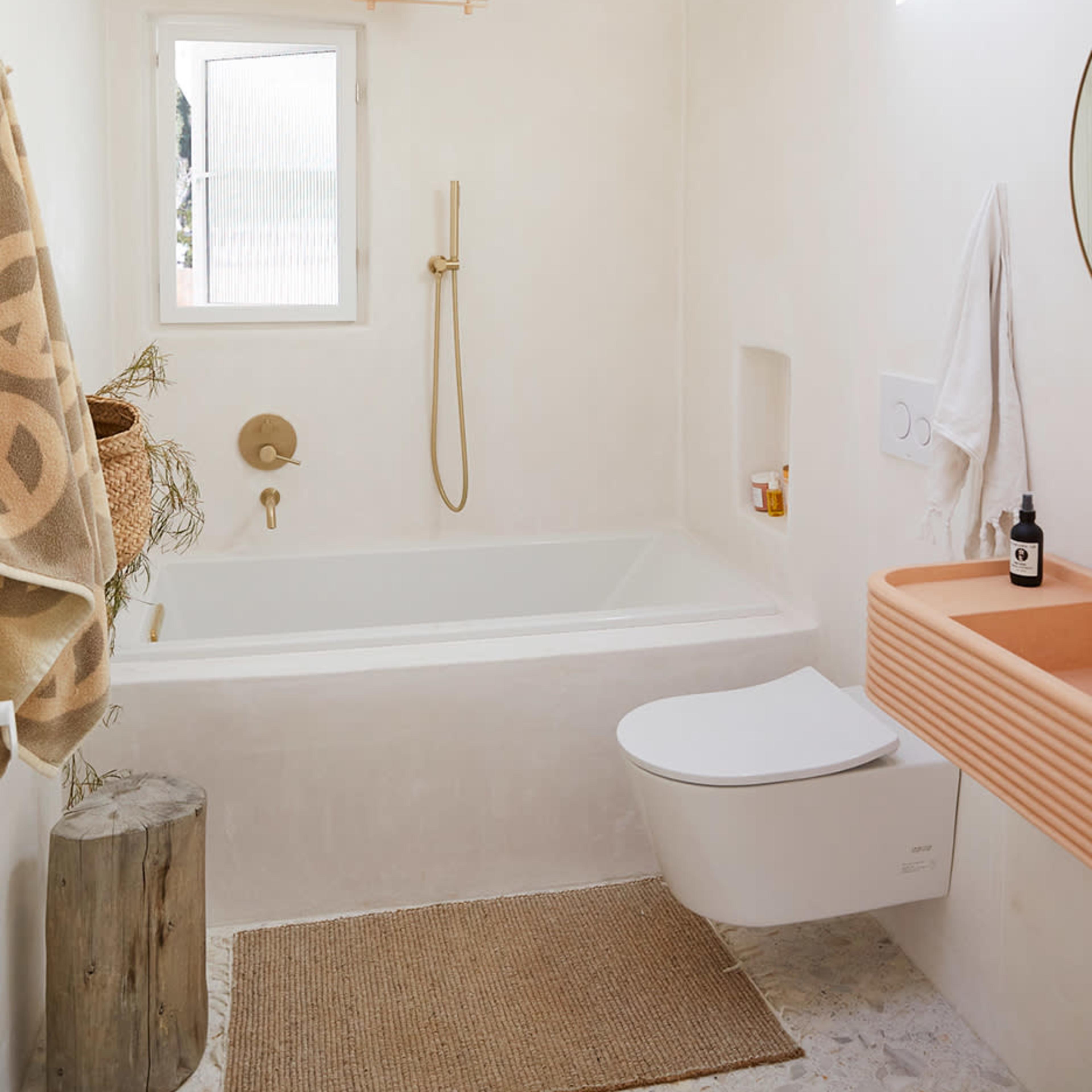 A minimalist bathroom featuring a bathtub, a wall-mounted sink with an orange countertop, and a light fixture hanging from the ceiling.