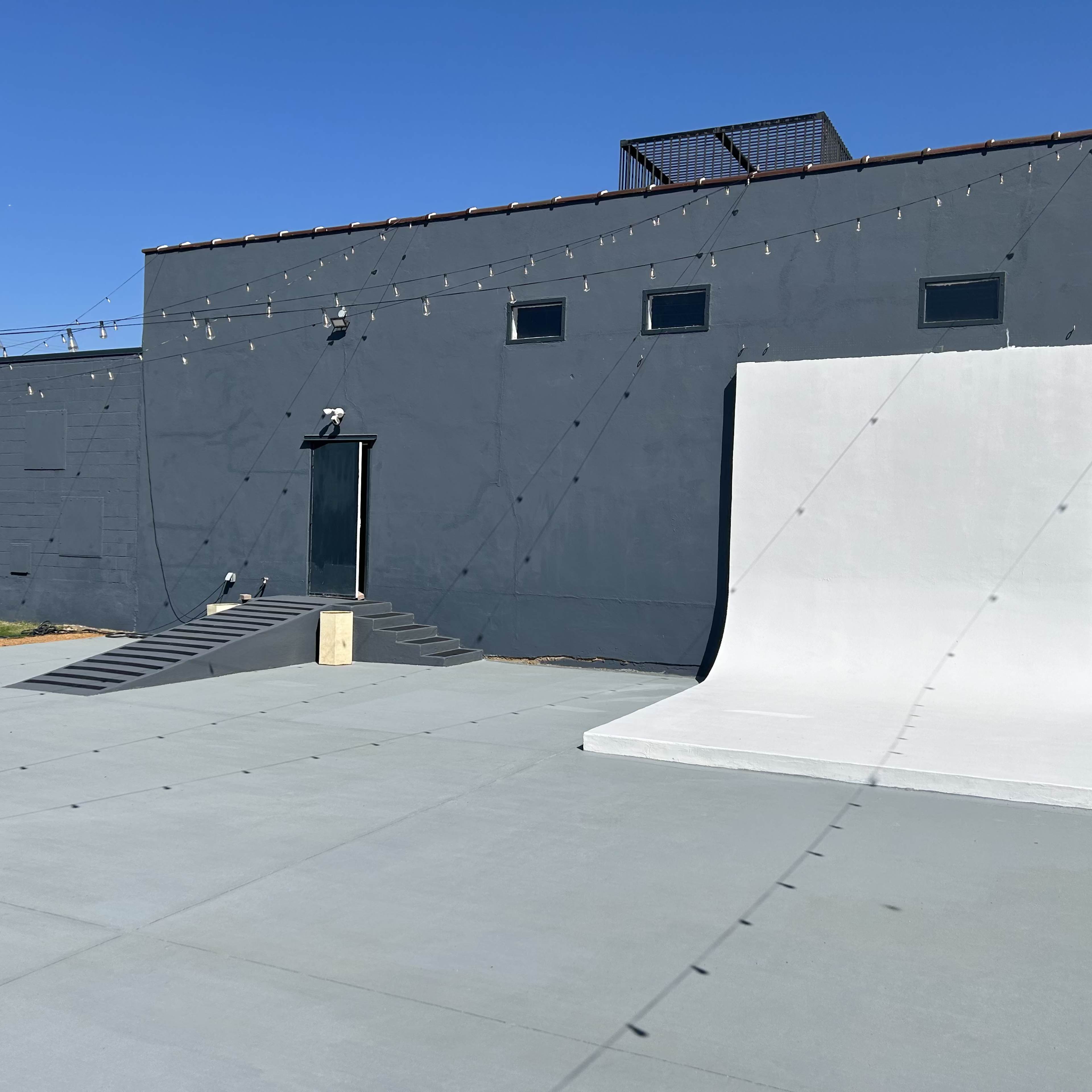 A concrete slab with a ramp leading to a gray wall, under a clear blue sky.