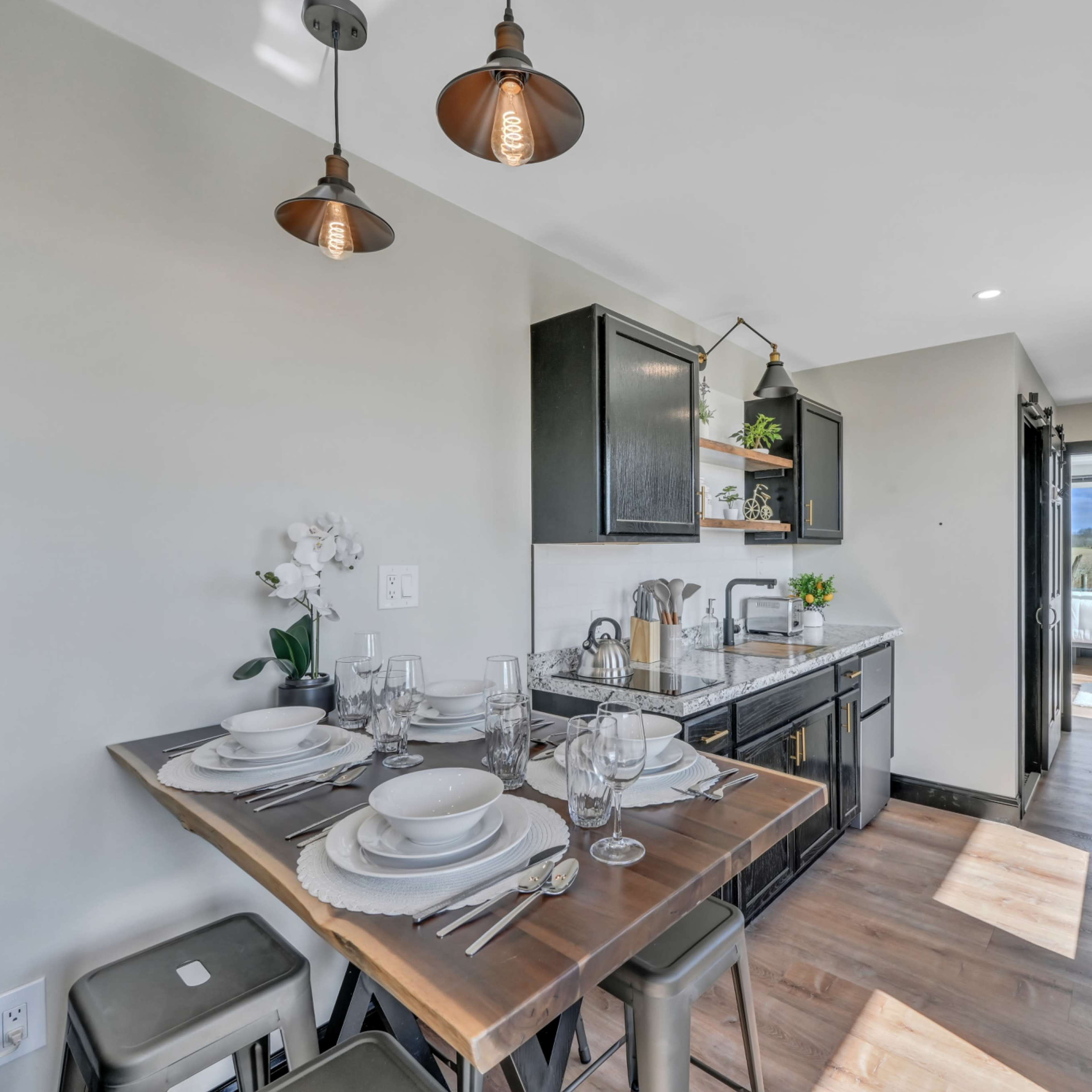 A modern kitchen and dining area features a wooden table set for four, ample counter space, and a sliding door opening to a scenic view.