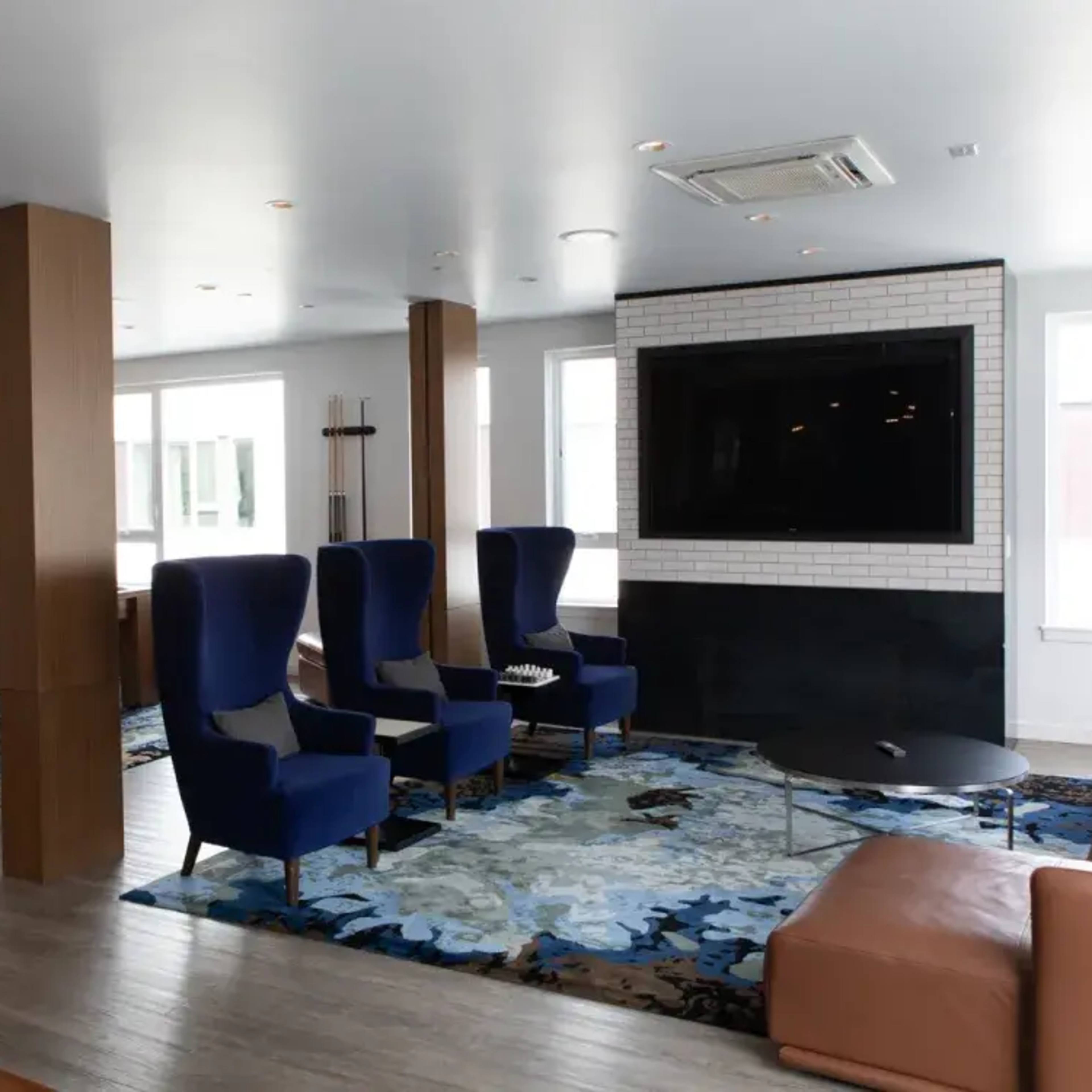A modern living space with a sectional sofa, two armchairs, a coffee table, a television mounted on the wall, and large windows.
