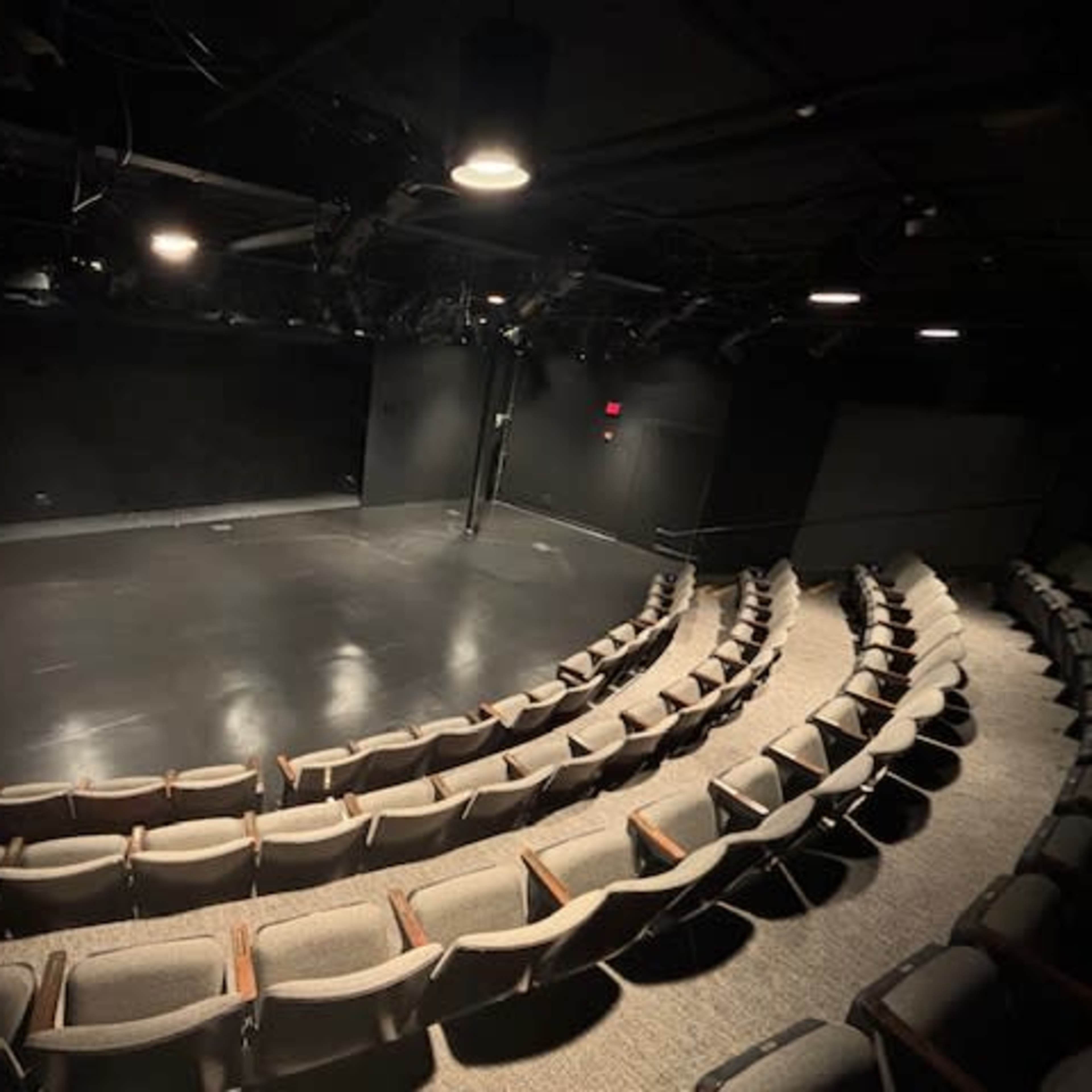 A black box theater with tiered seating and a clear performance stage at the front.
