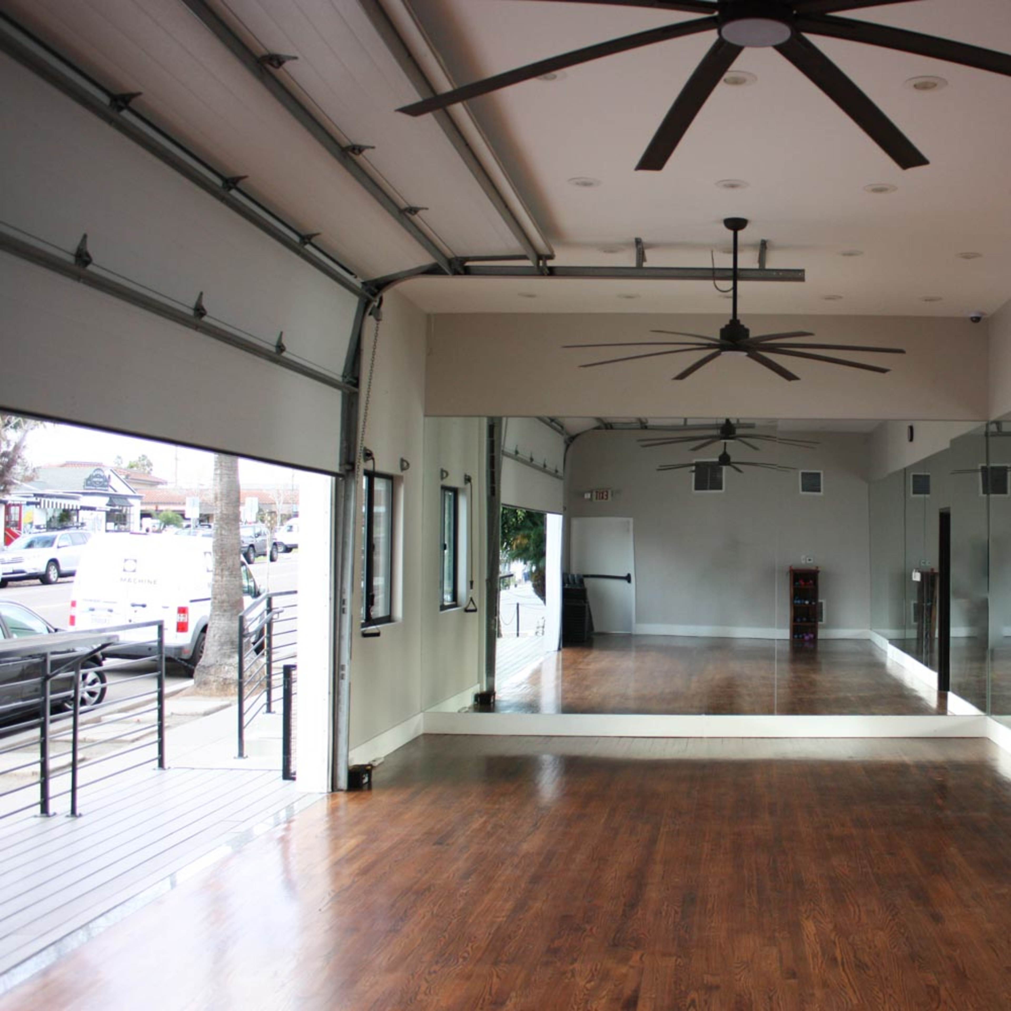 A spacious room with hardwood floors, large mirrors on one wall, and a ceiling featuring multiple overhead fans.