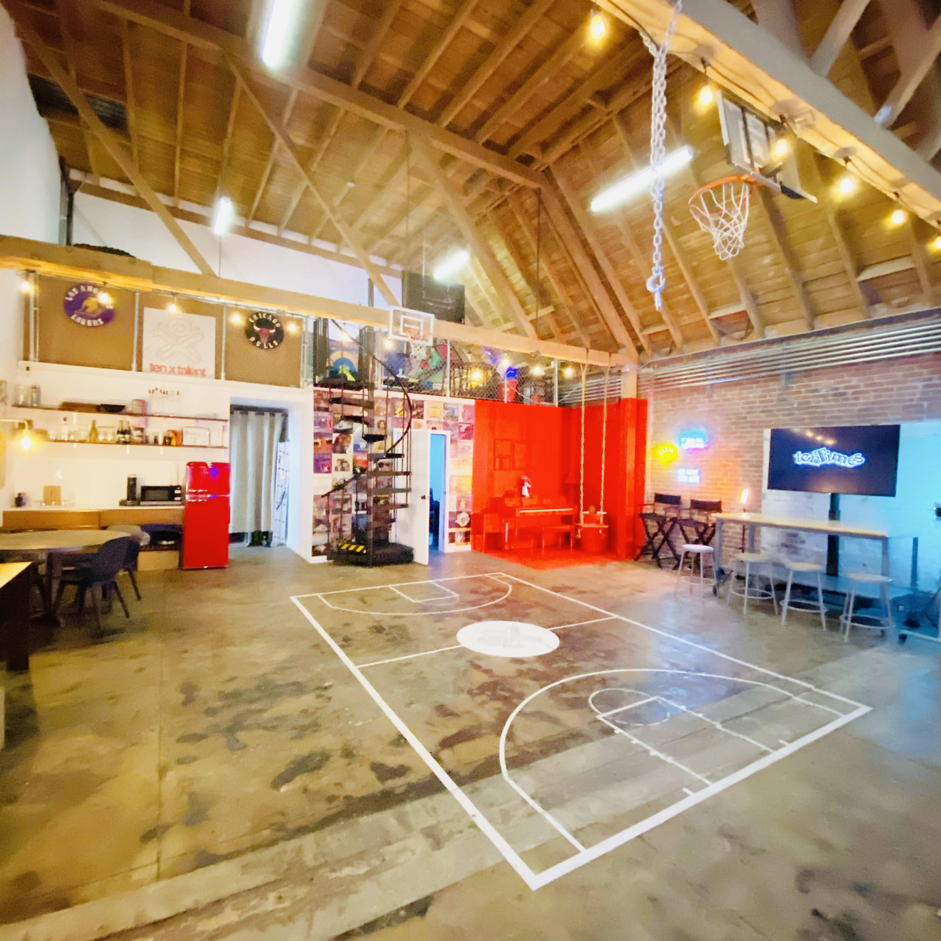 An indoor space with a basketball court design on the floor, surrounded by seating areas and decorative elements, under a high wooden ceiling.