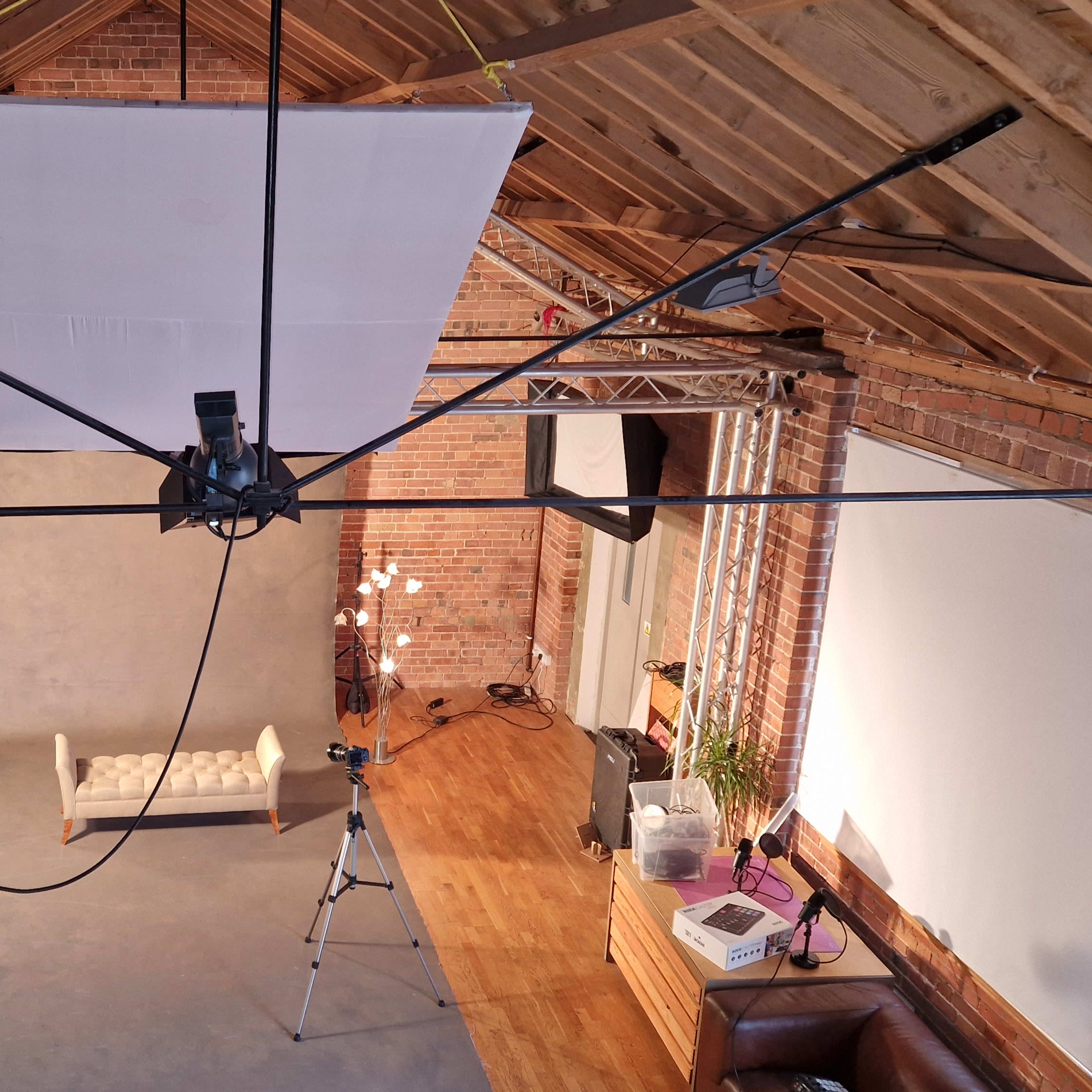 A photography studio features a wooden ceiling, multiple lighting setups, and a gray backdrop in front of a sofa.