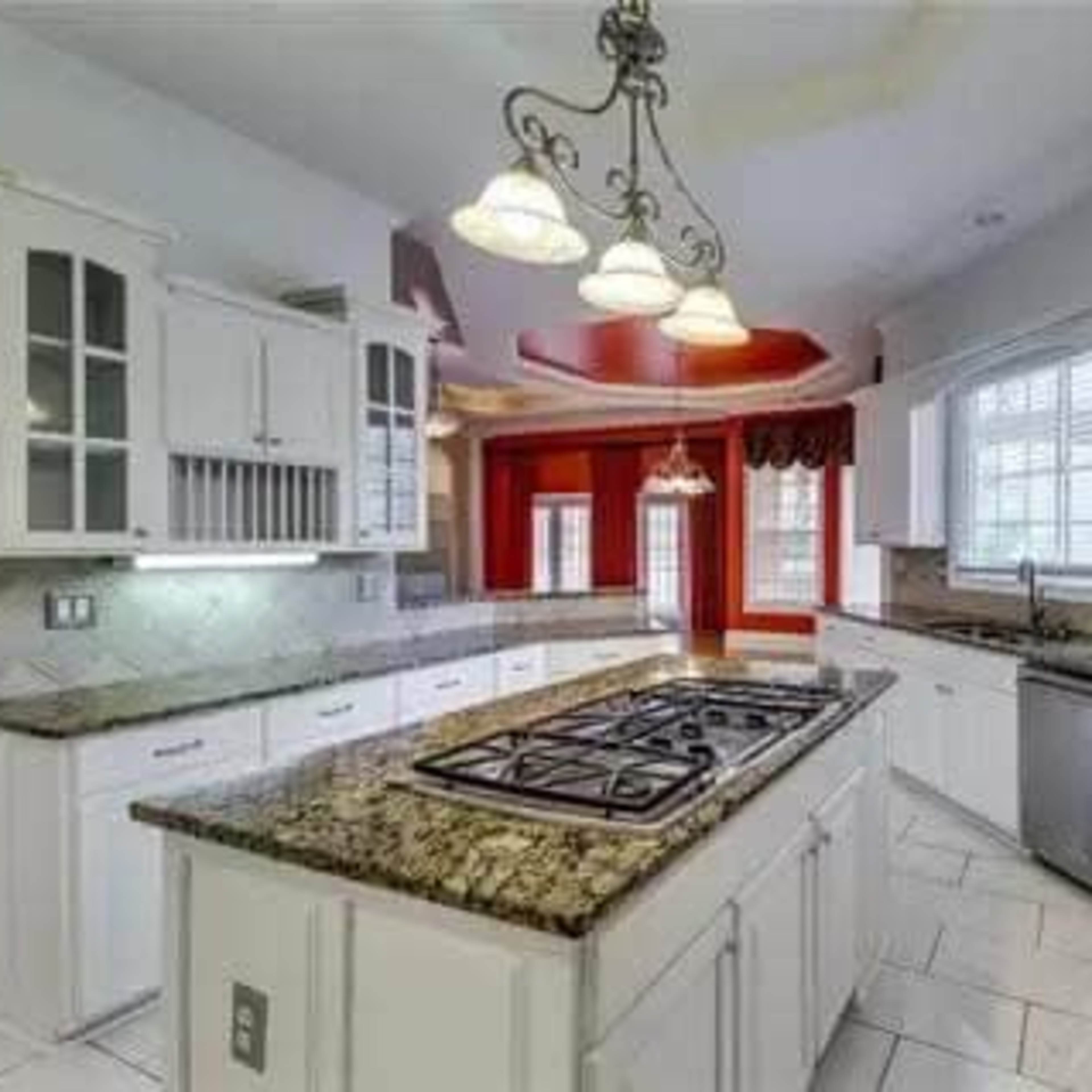 A modern kitchen with white cabinetry, a central island with a gas stove, and granite countertops.