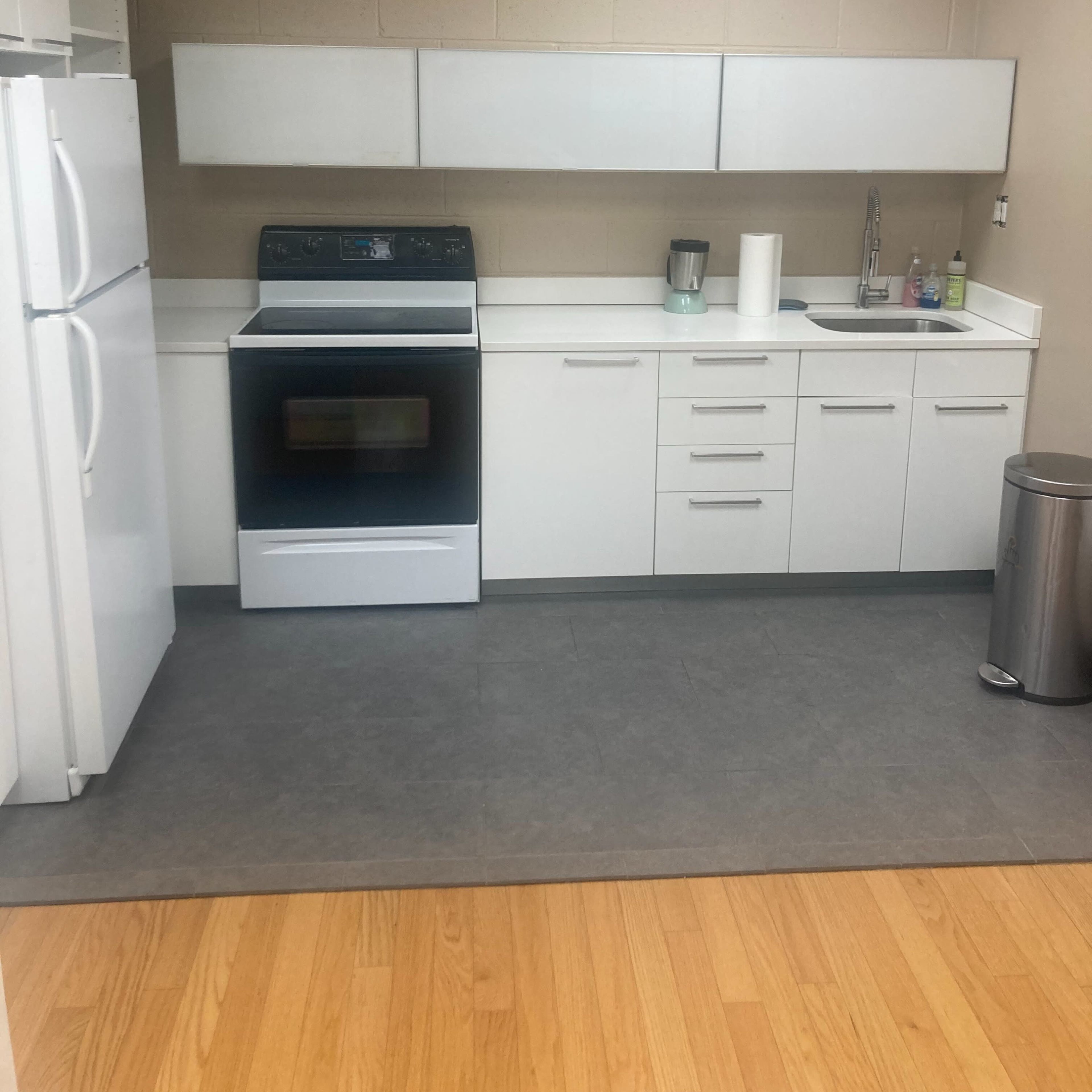 A modern kitchen with white cabinetry, a black oven, and a refrigerator, featuring a sink and minimal countertop appliances.