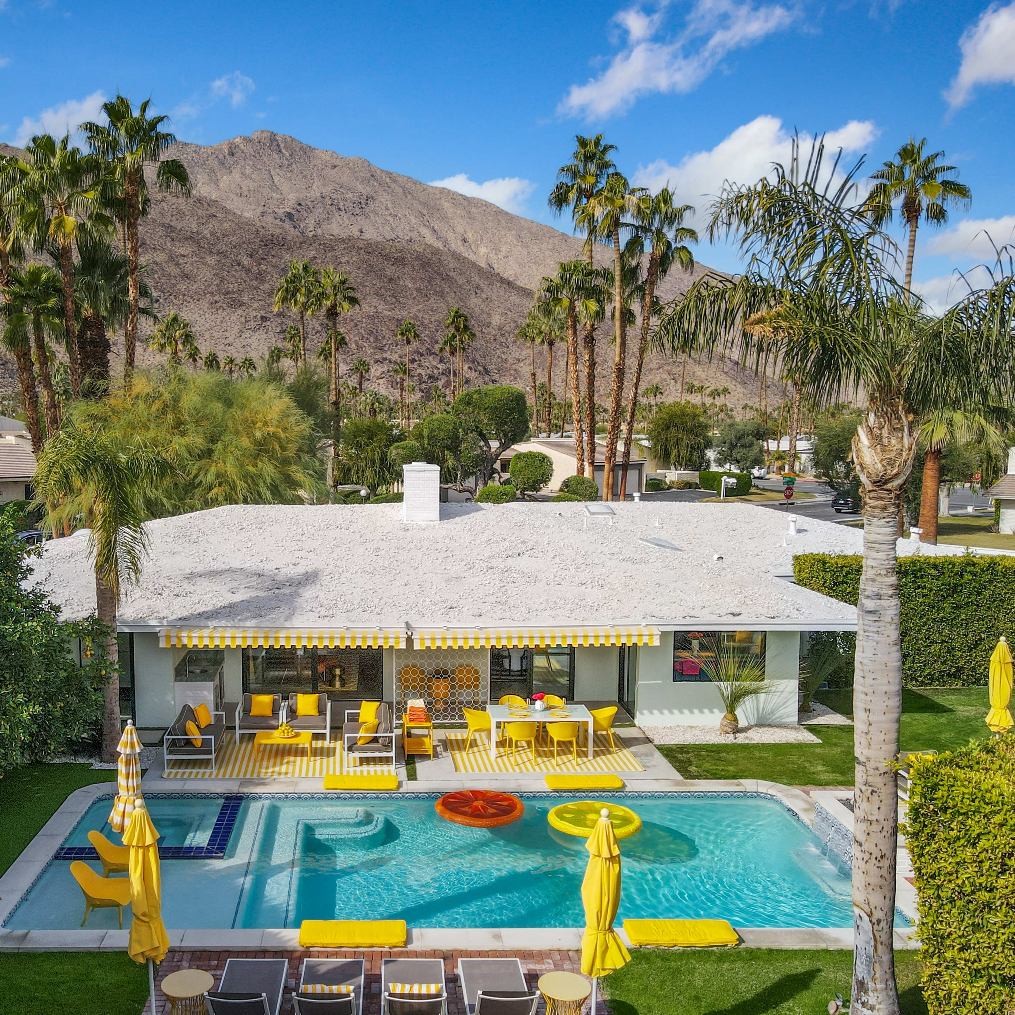 A modern house with a pool is surrounded by palm trees and mountains in the background.