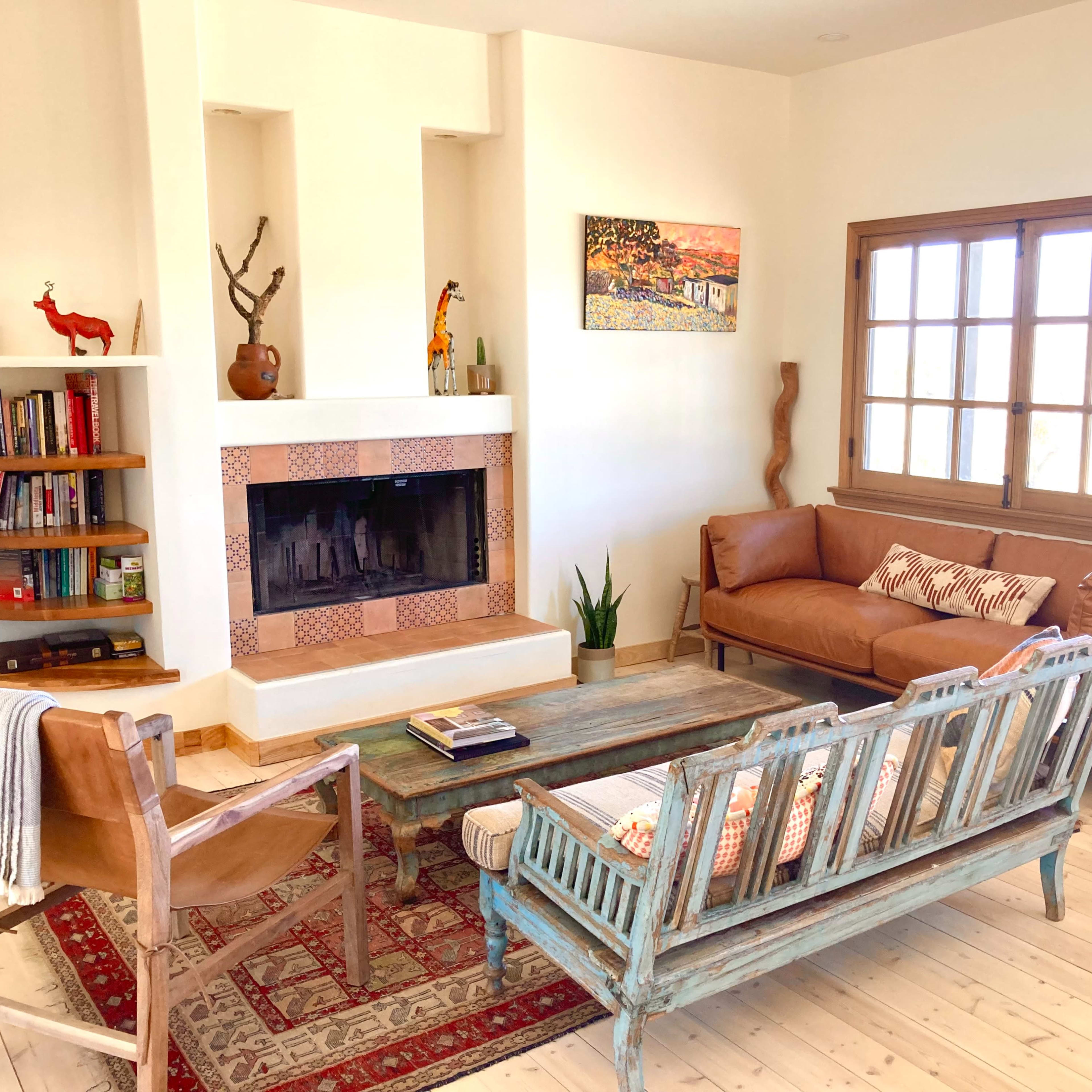 A well-lit living room with a fireplace, a wooden coffee table, two leather sofas, and a bookshelf filled with books.