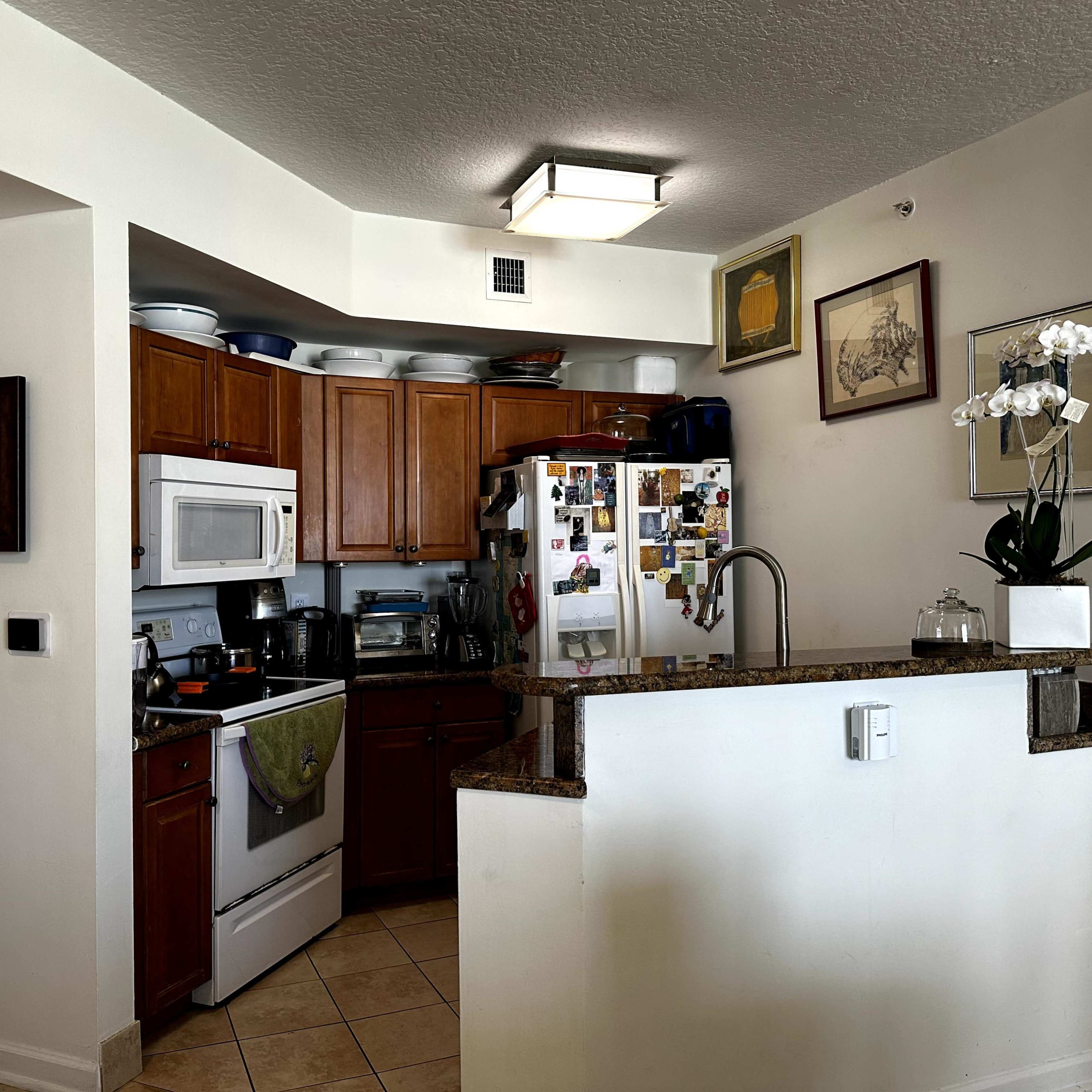 A compact kitchen with wooden cabinets, stainless steel appliances, and a small bar that opens to the living space.