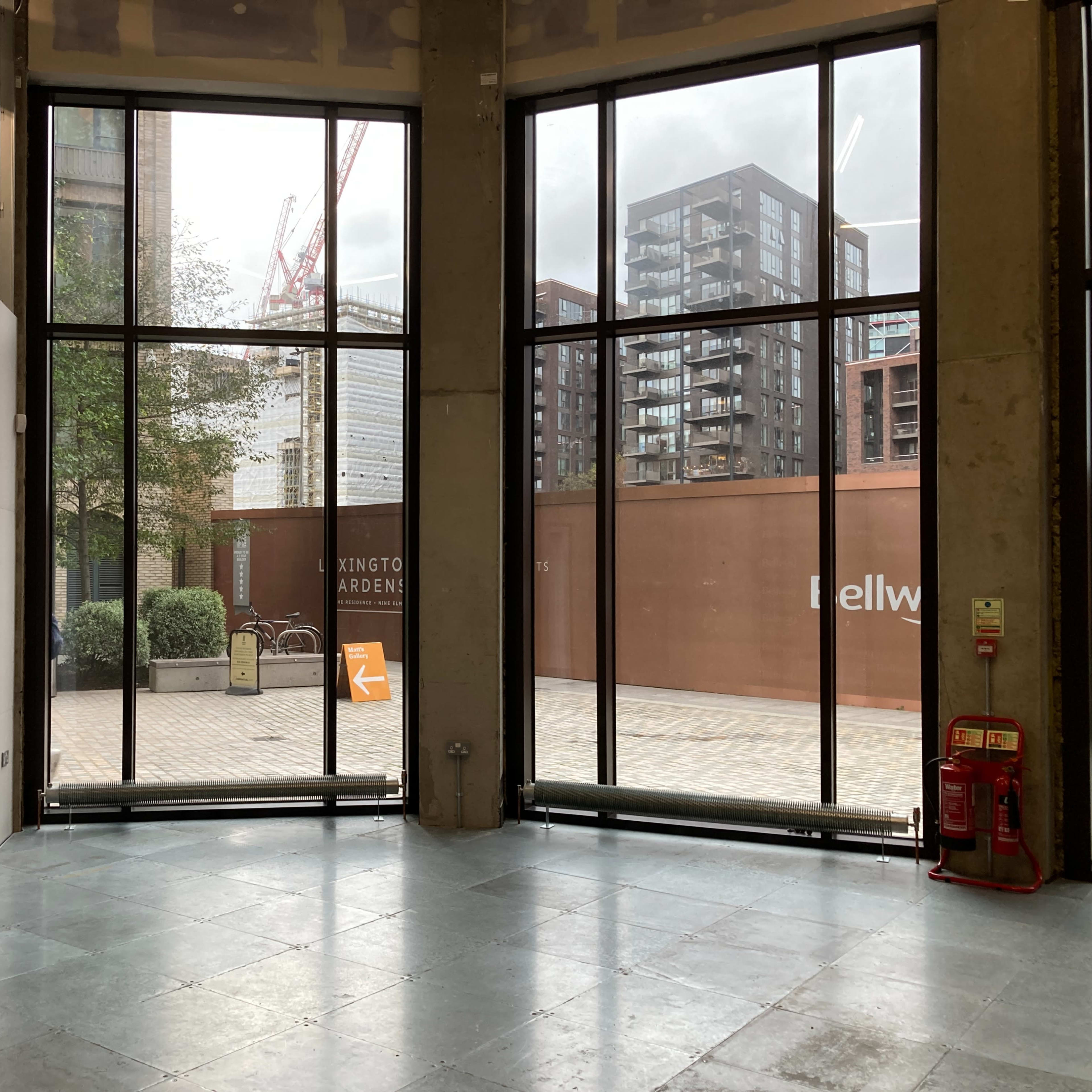 A spacious interior with large glass windows overlooking a paved outdoor area and modern buildings.