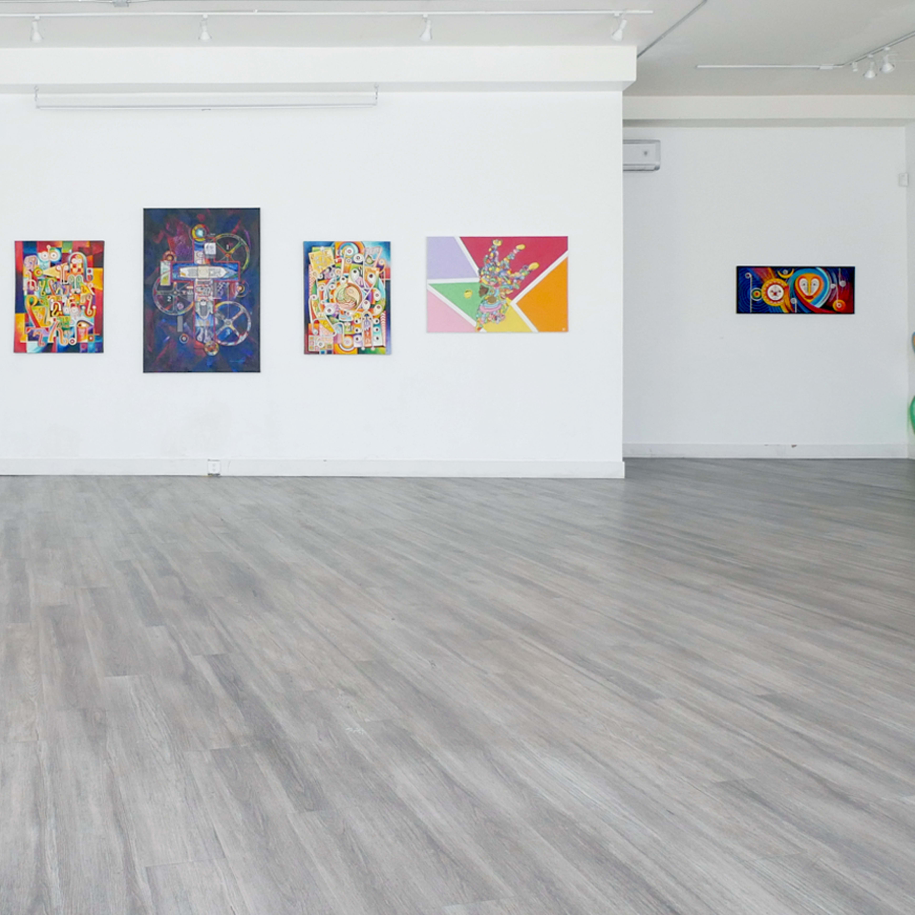 A brightly lit art gallery featuring colorful paintings on the walls and a spacious wooden floor.