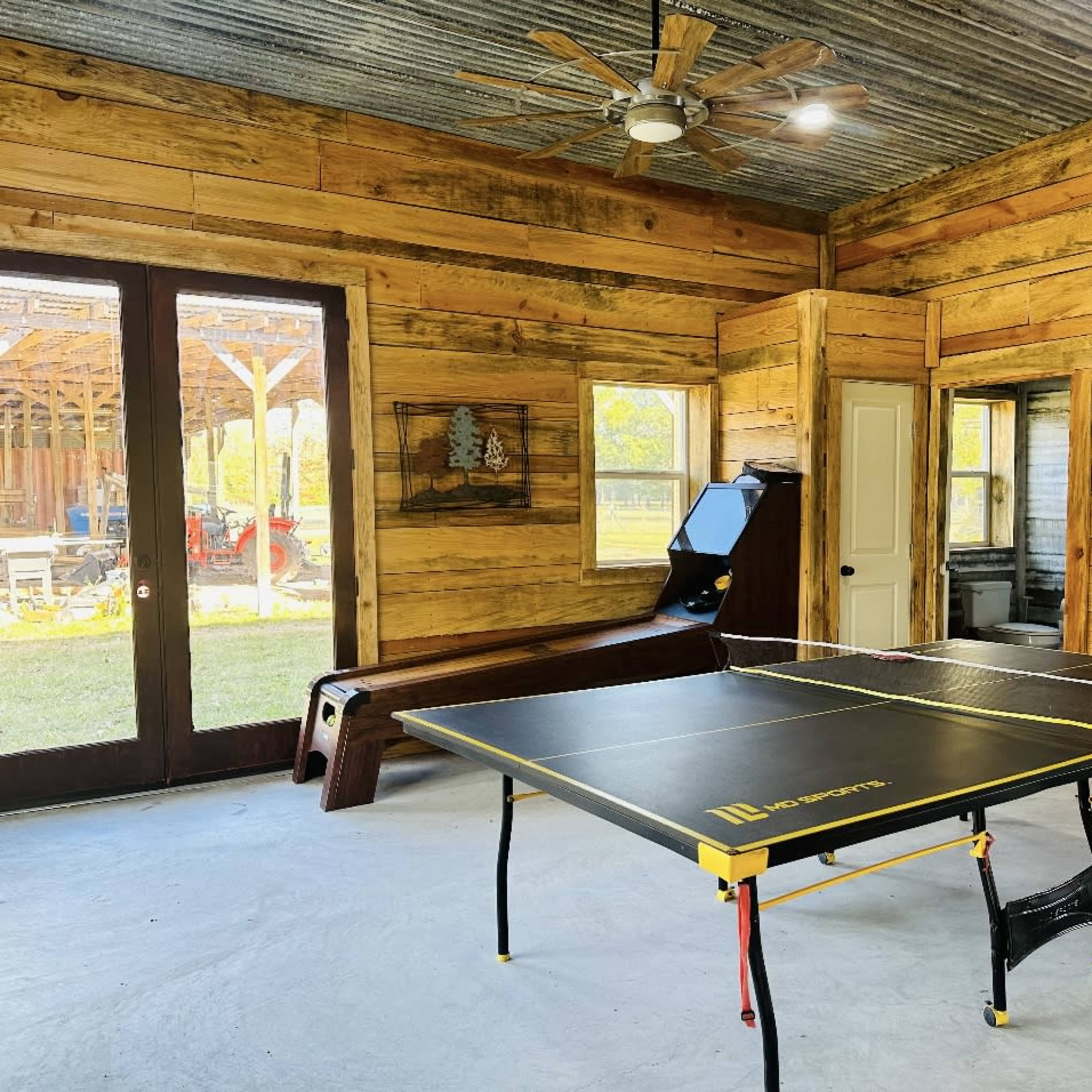 A wooden cabin interior featuring a ping pong table, a dartboard setup, and a ceiling fan.