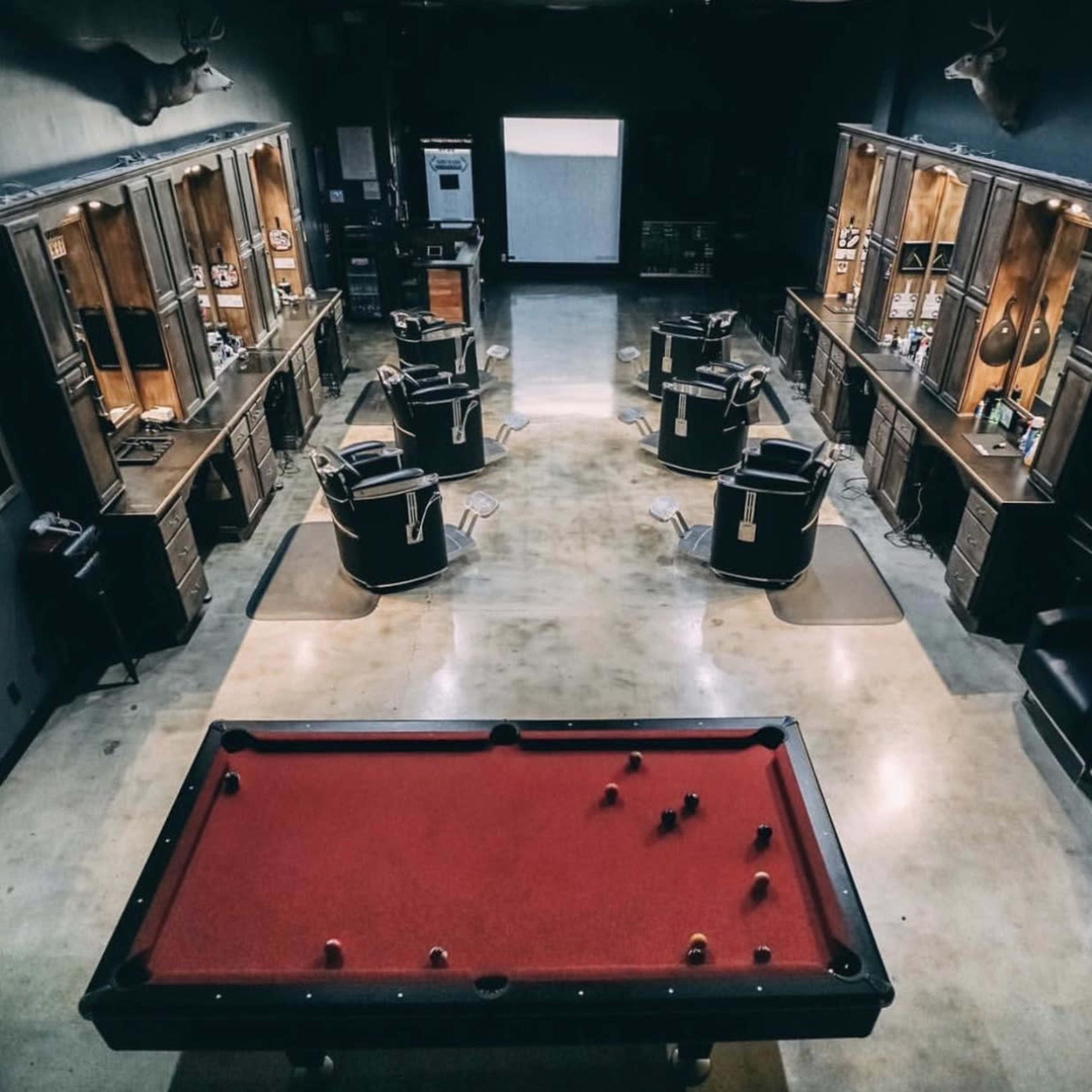 A vintage barbershop interior with several barber chairs, a pool table, and wooden cabinetry lining the walls.