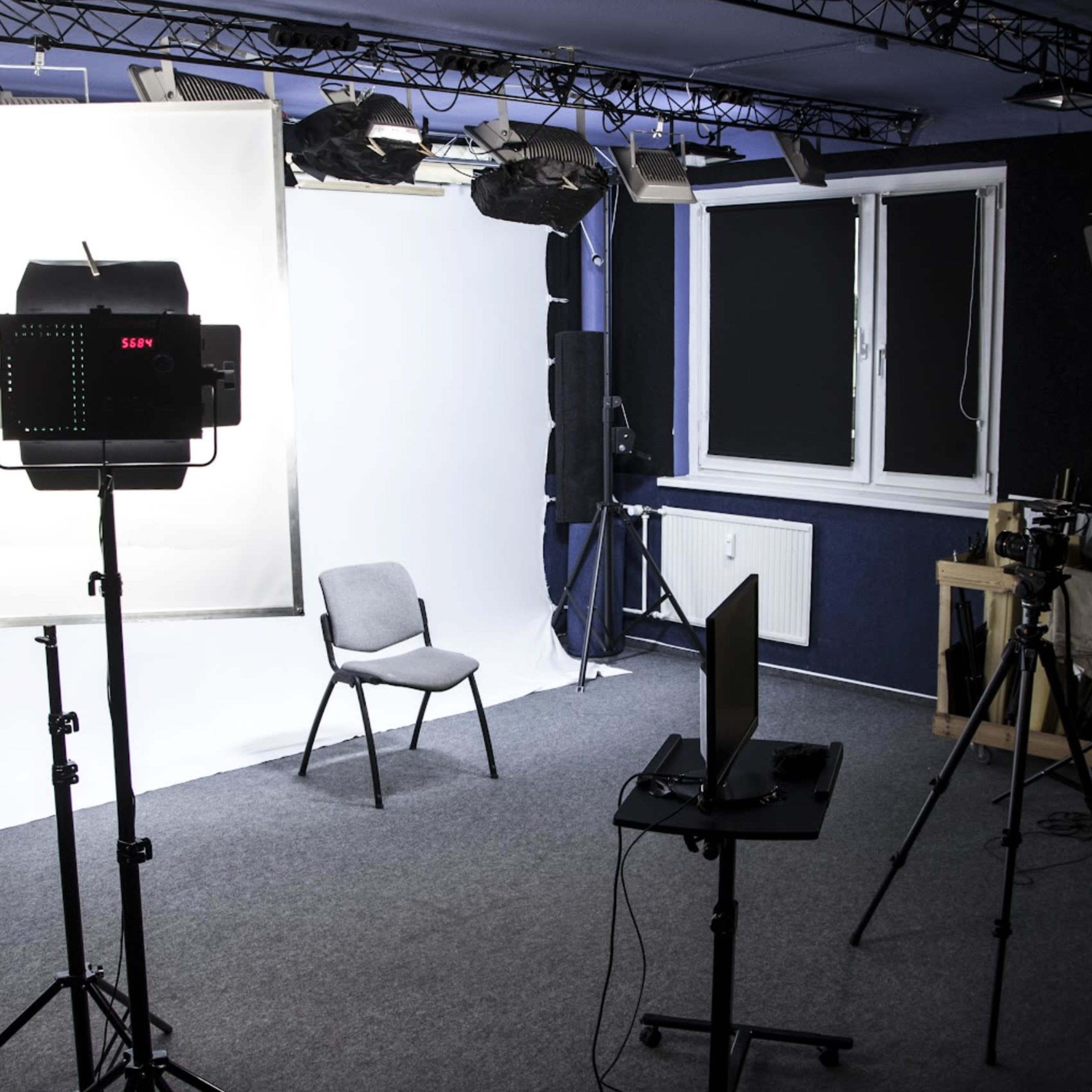 A well-equipped studio space features a backdrop, lighting equipment, a chair, and various cameras set up for recording.
