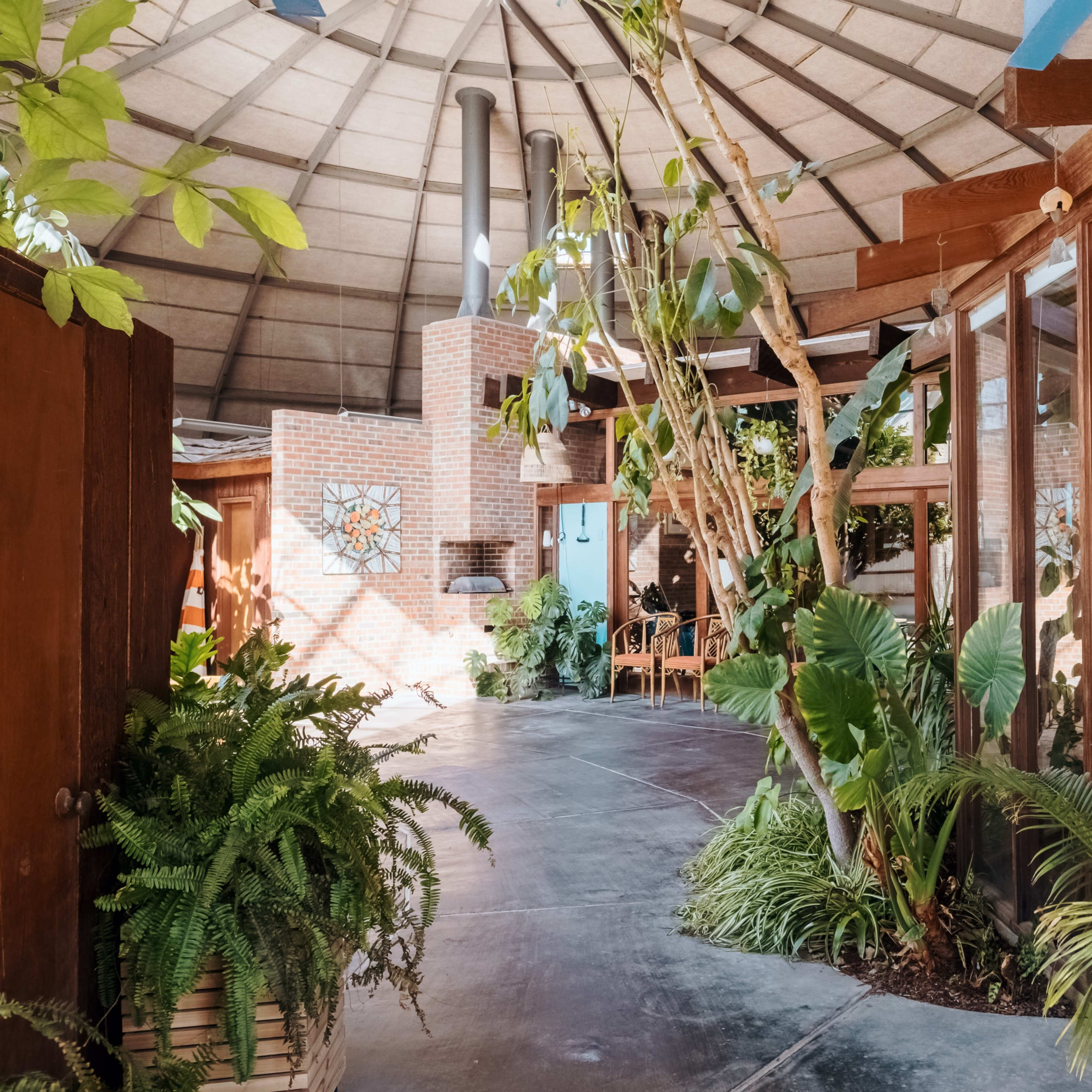 A circular interior space with wooden beams, large glass windows, and various plants integrated into the design.