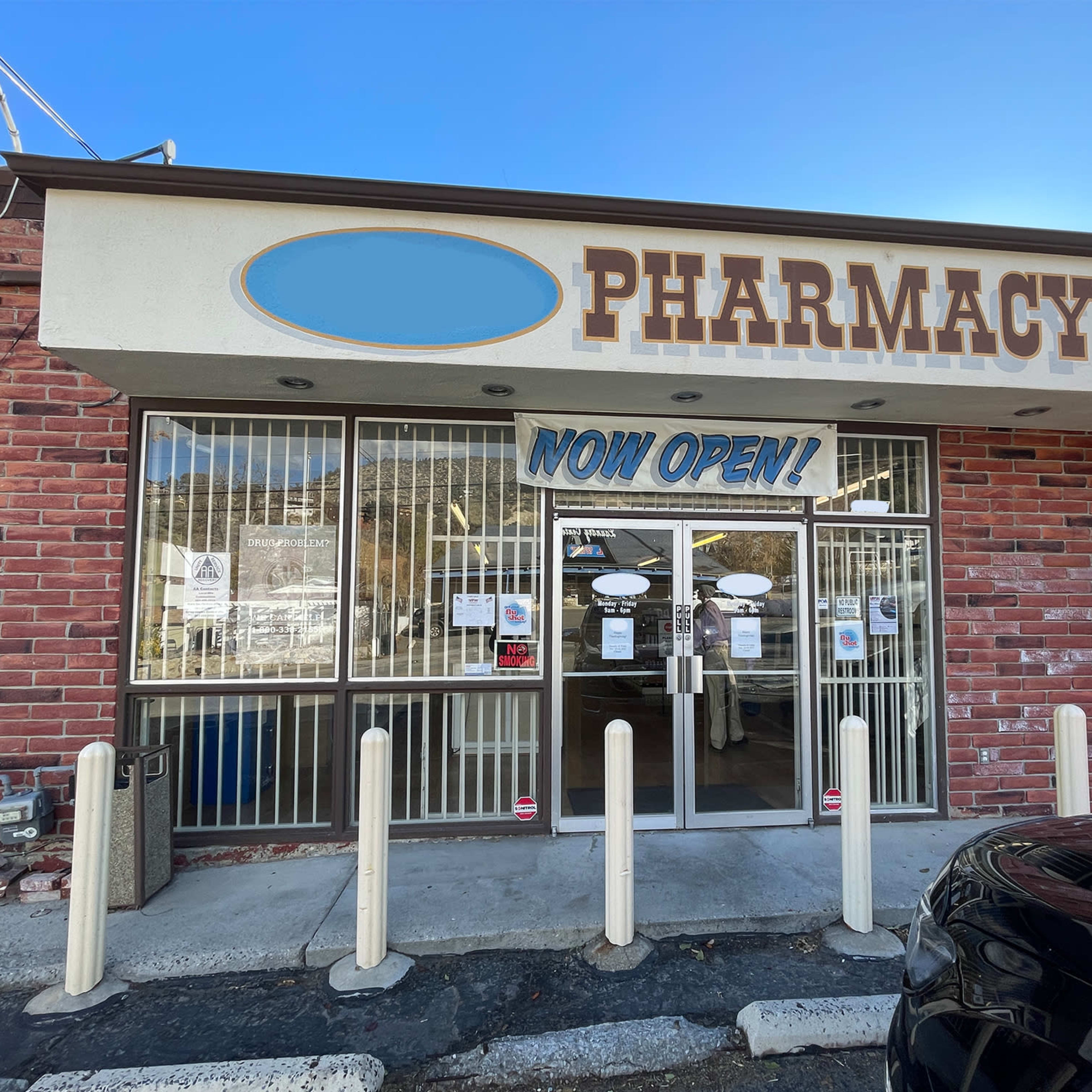 A pharmacy storefront with a large "NOW OPEN!" sign displayed in the front window.