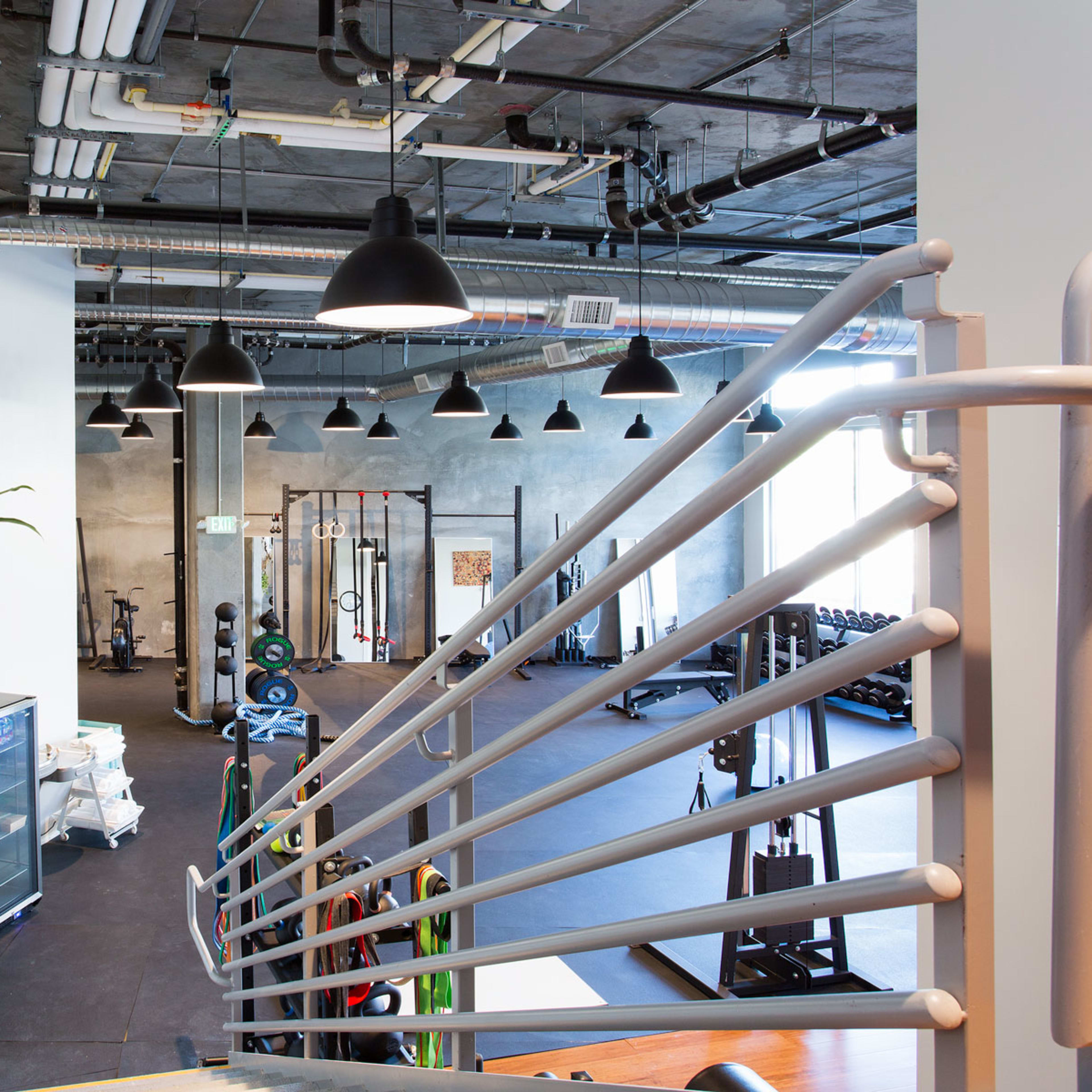 The interior of a modern gym with exercise equipment and a staircase in the foreground.