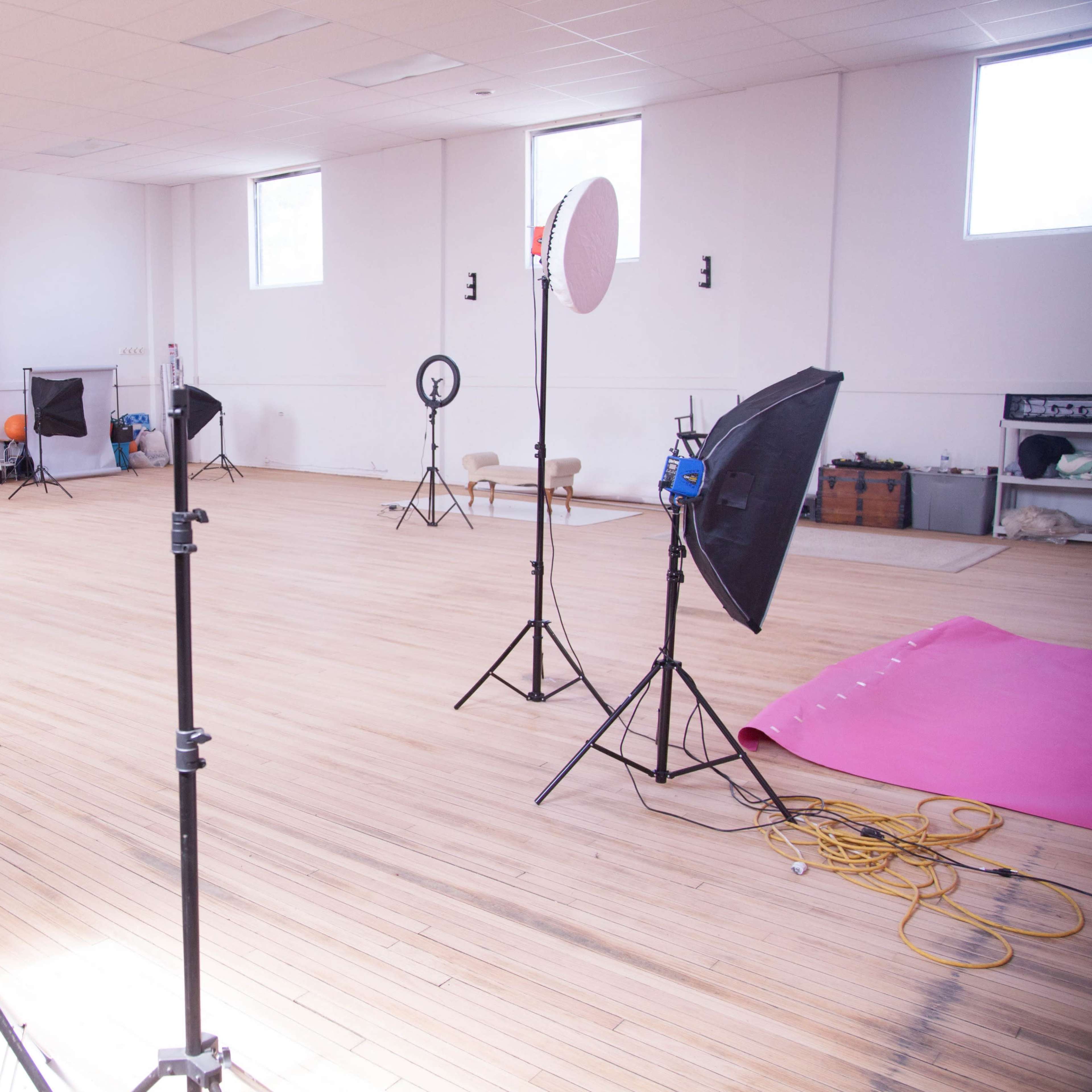 A spacious, empty photography studio with various lighting equipment and backdrops set up around a wooden floor.