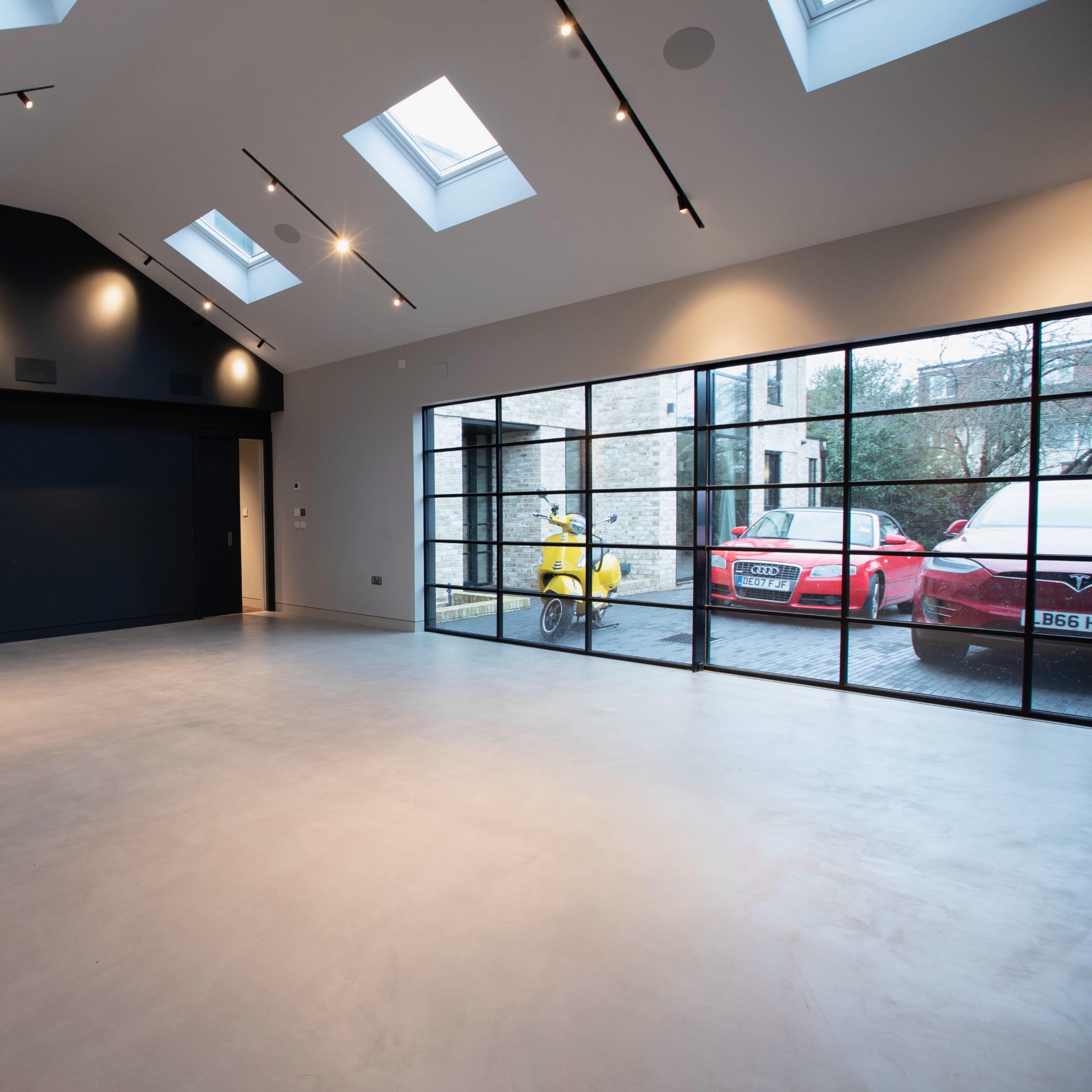 A spacious, modern interior with a concrete floor, large windows, and skylights illuminating the room.