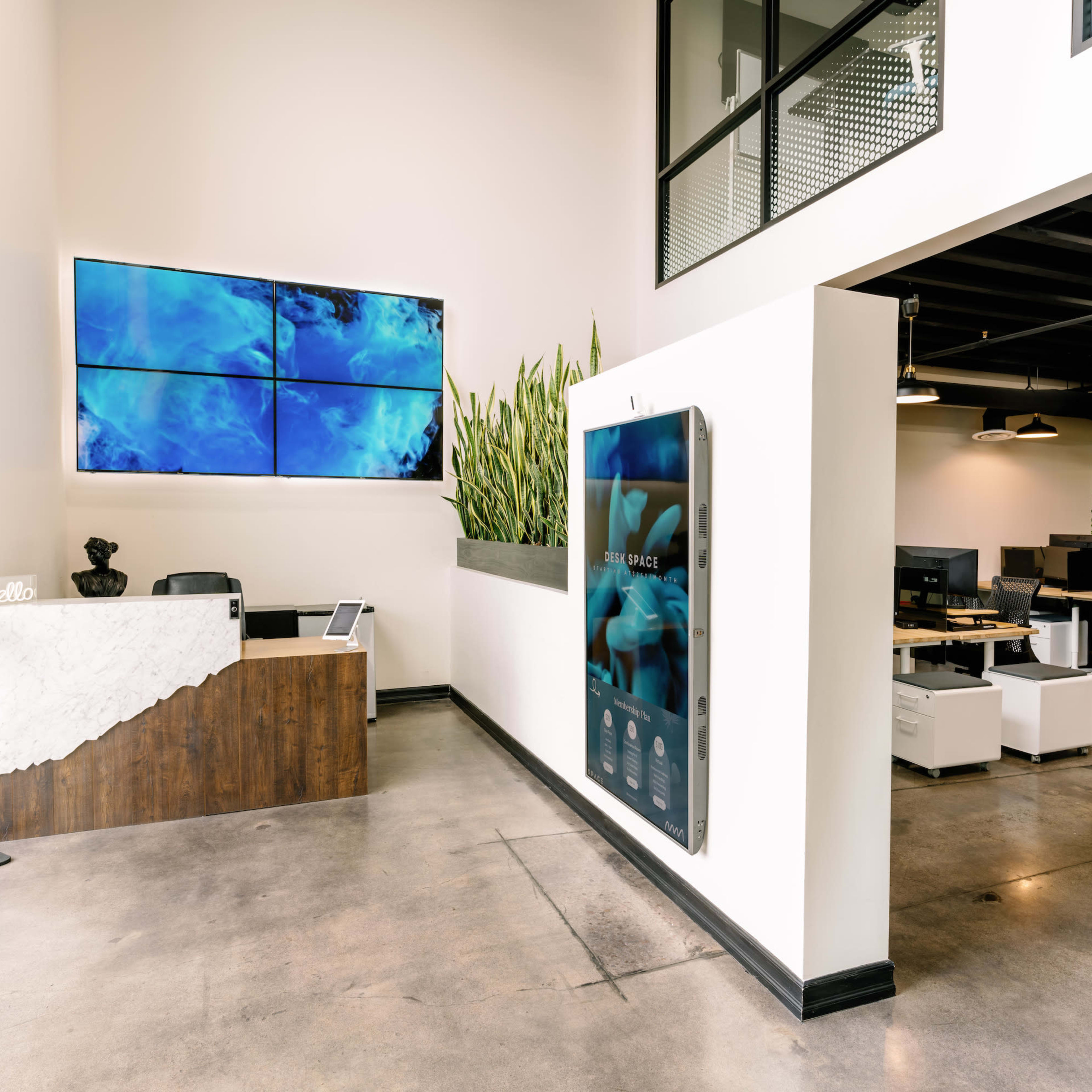 A modern office reception area with sleek furniture, a large digital screen, and greenery accenting the walls.