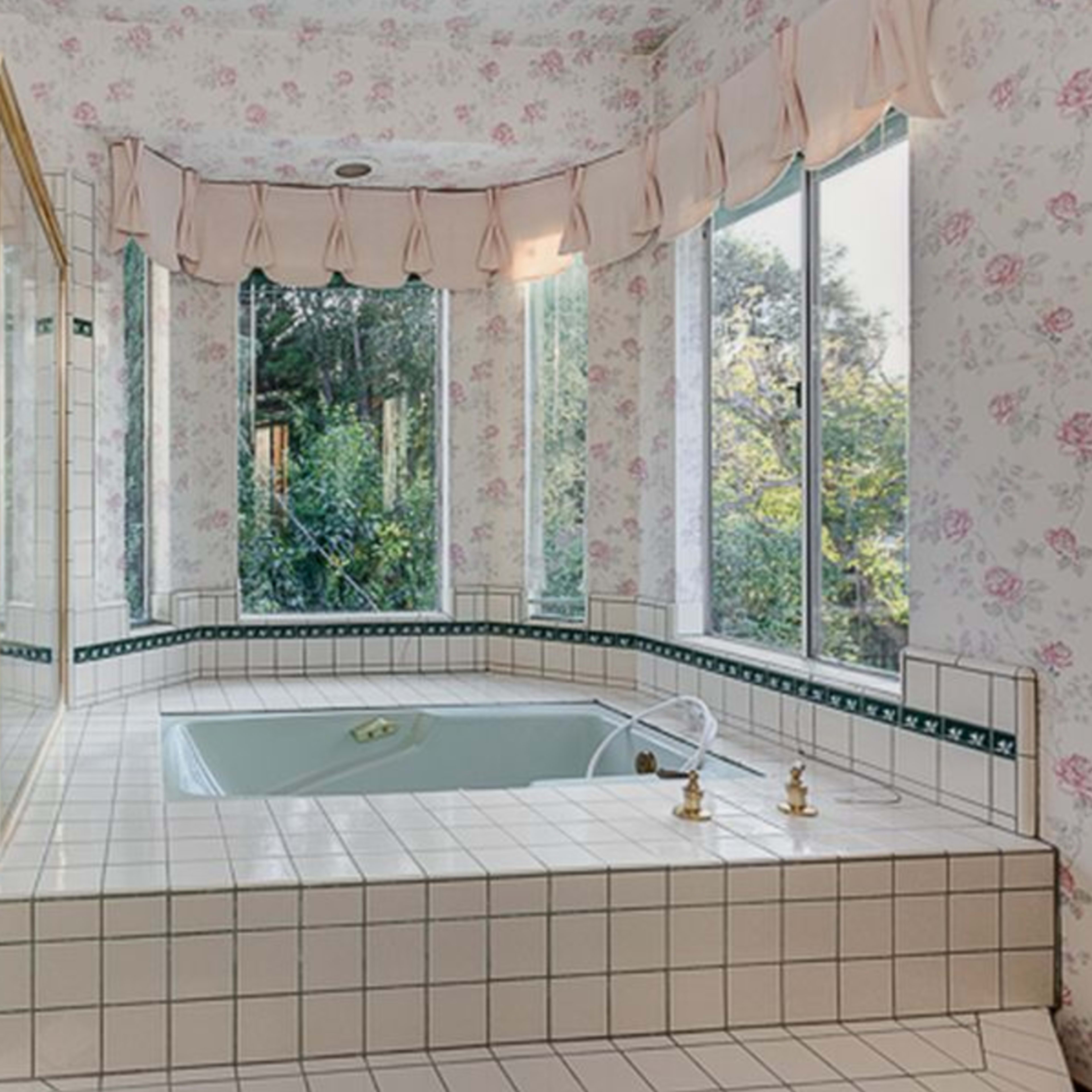 The bathroom features a large corner jacuzzi tub and a glass-enclosed shower, surrounded by floral wallpaper and multiple windows.