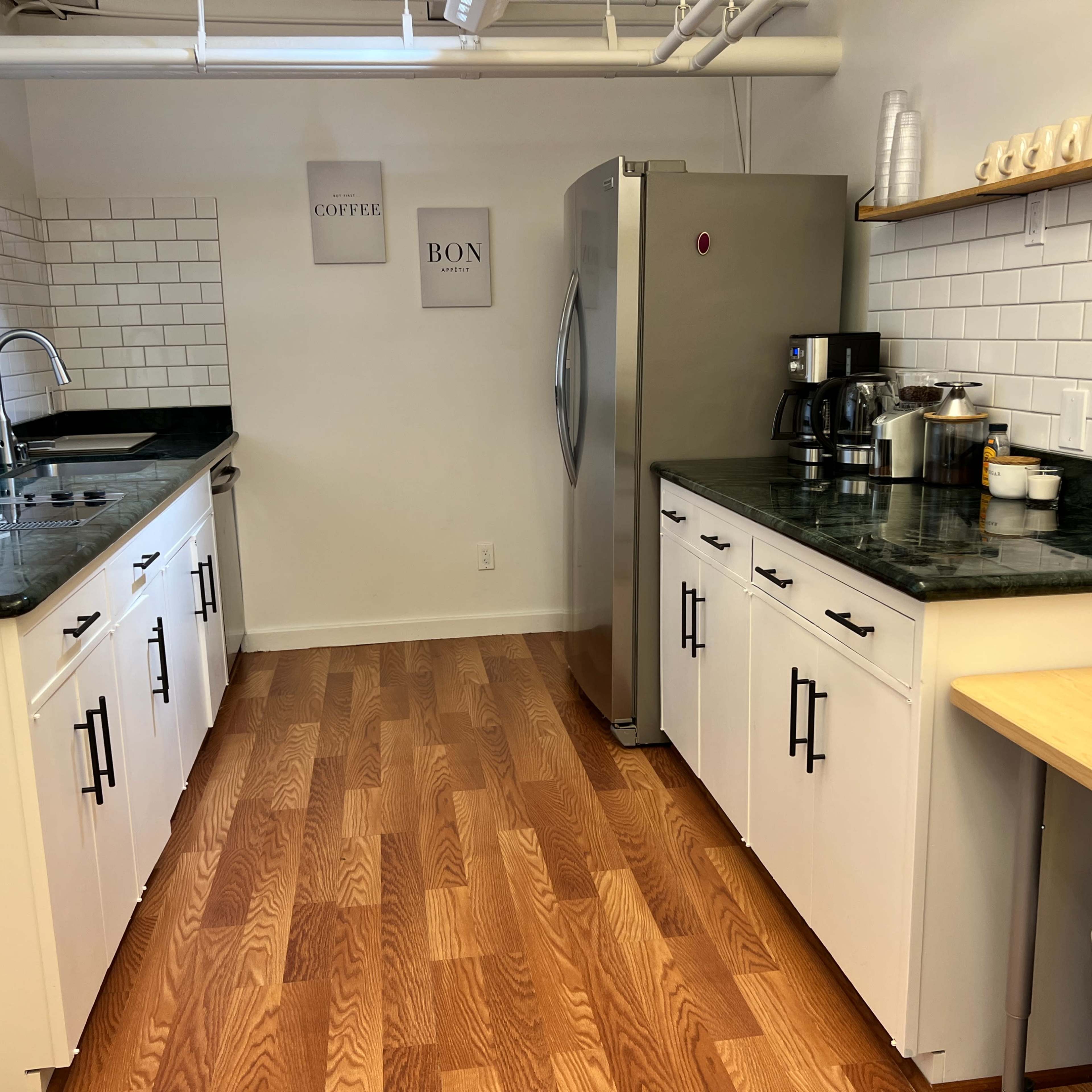 A tidy kitchen with white cabinets, dark countertops, stainless steel appliances, and wooden floors.
