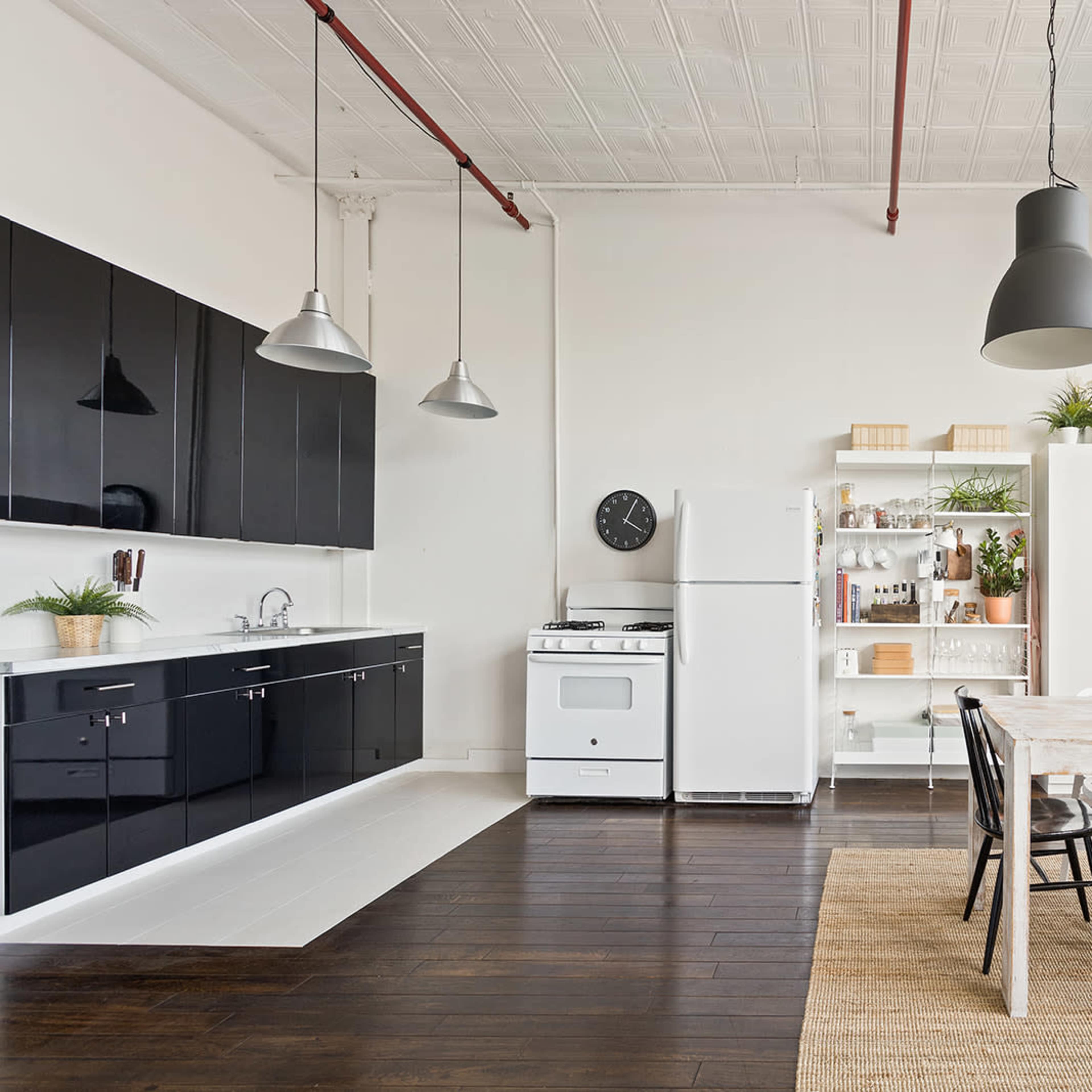 A modern kitchen with black cabinetry, a white stove, and a dining area featuring a large wooden table surrounded by black and white chairs.