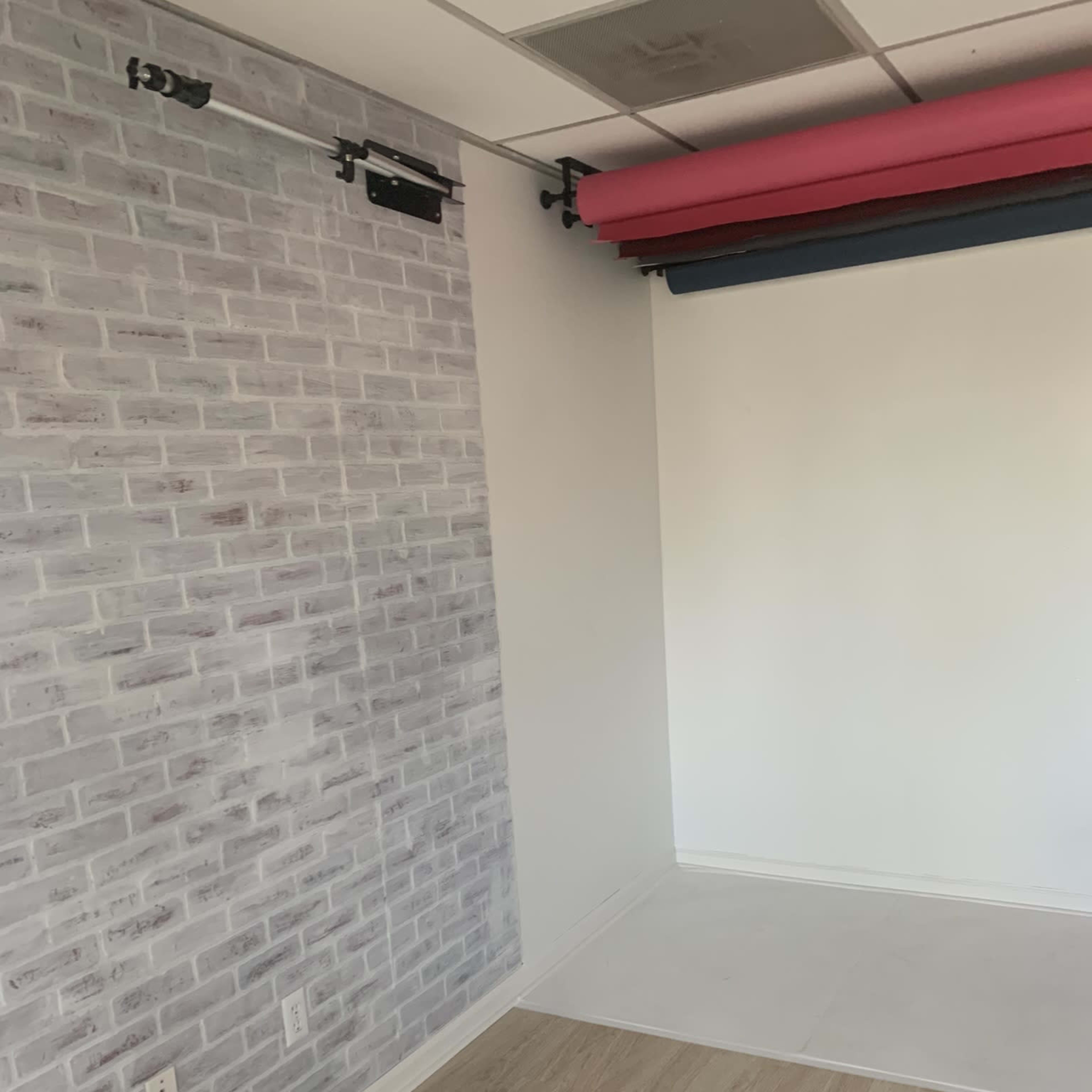 A room with a brick-patterned wall on one side, a plain white wall on the other, and a light wooden floor.