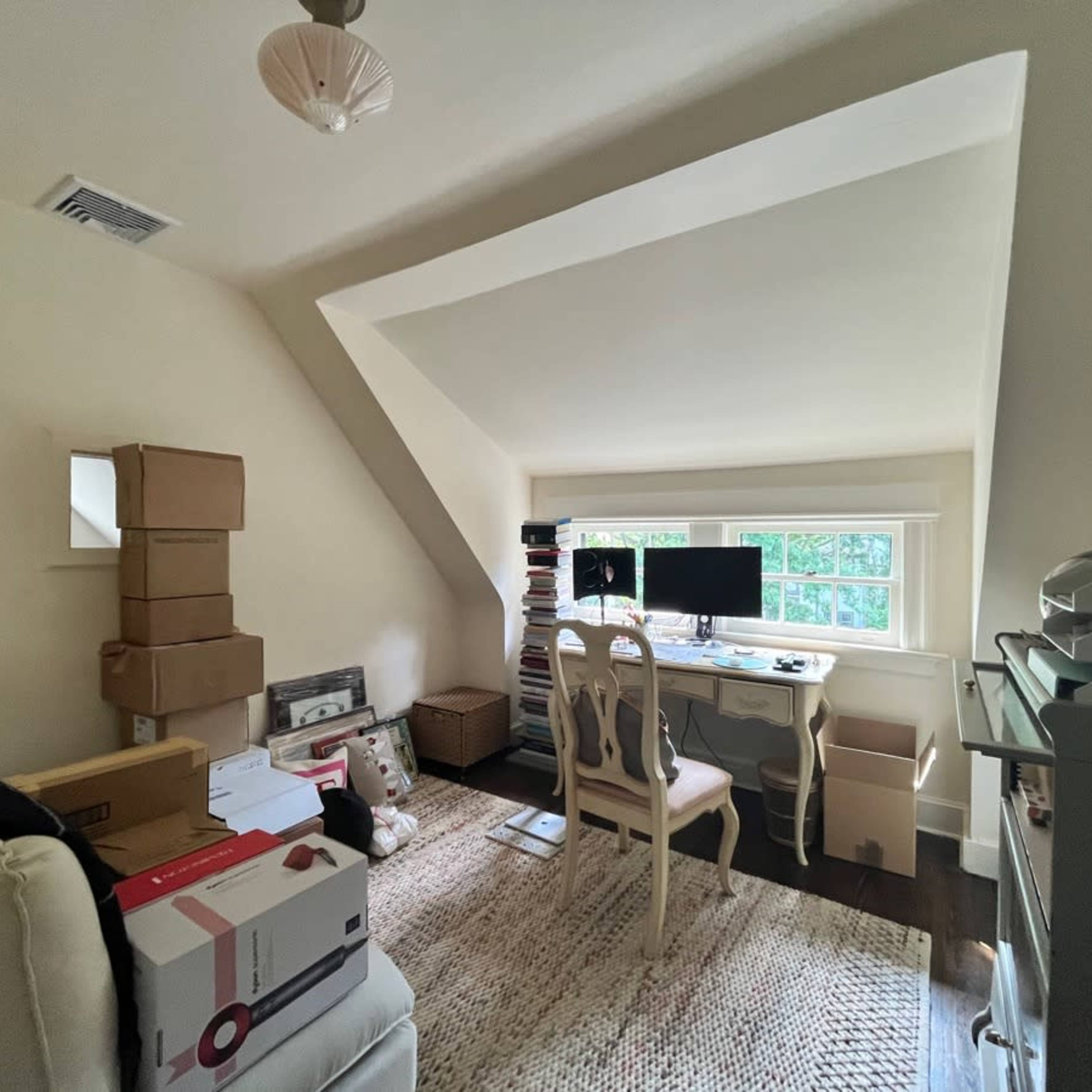 A neatly organized attic office space features a desk with two monitors, a chair, and stacked boxes along one wall.