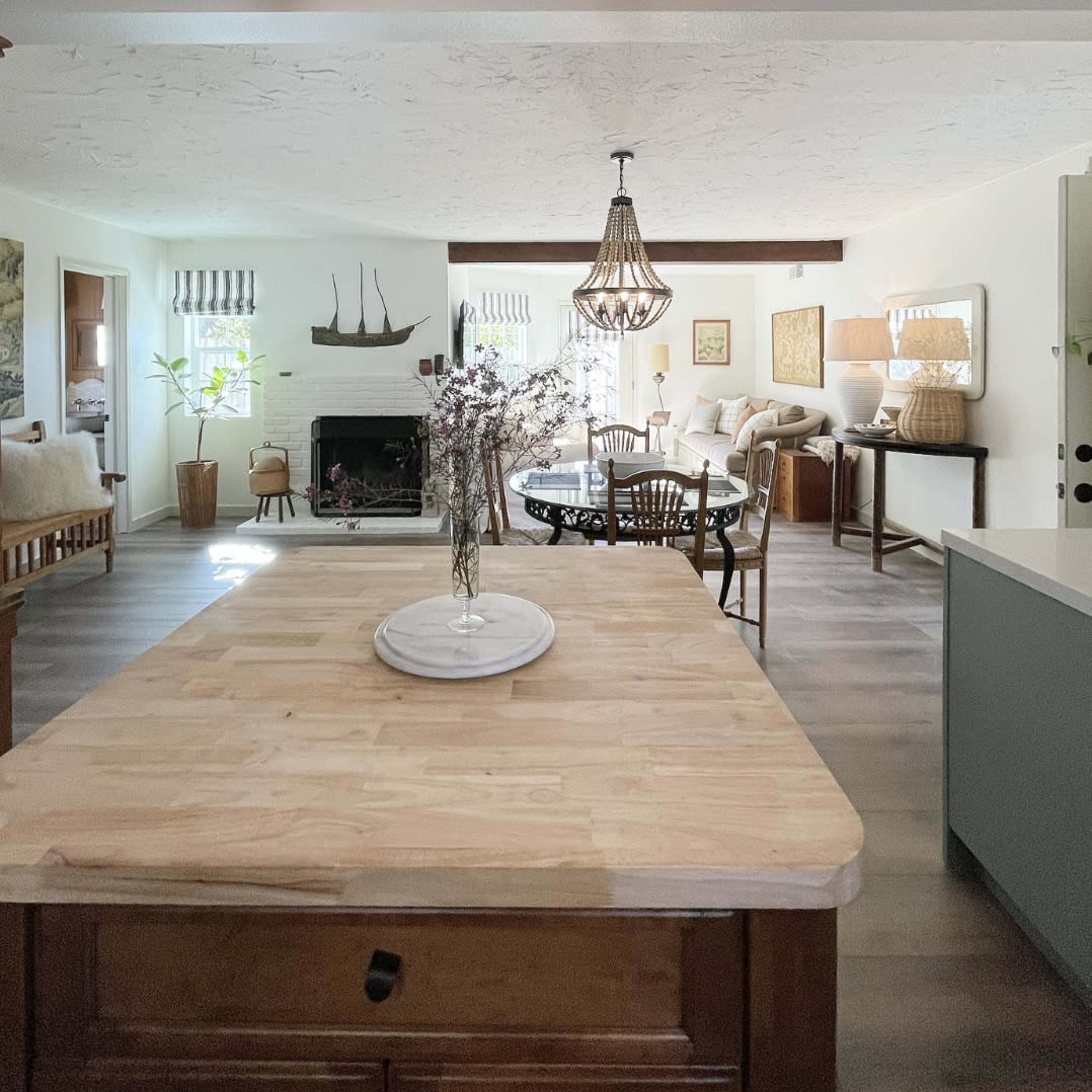 A wooden kitchen island is centered in a brightly lit open-concept living space that includes a dining area, seating area, and a fireplace.